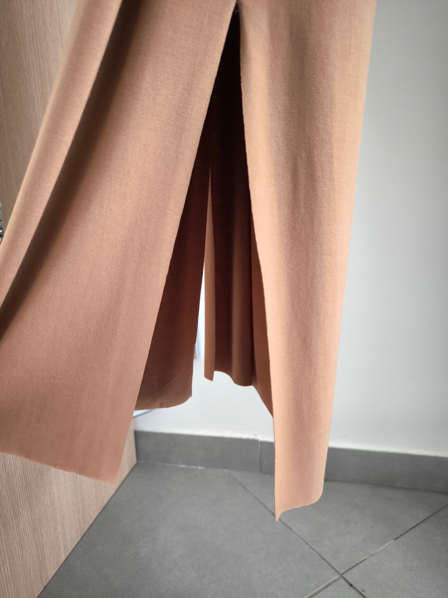 Abito lungo beige elegante con arricciature laterali e due spacchi, appeso su gruccia in una boutique.