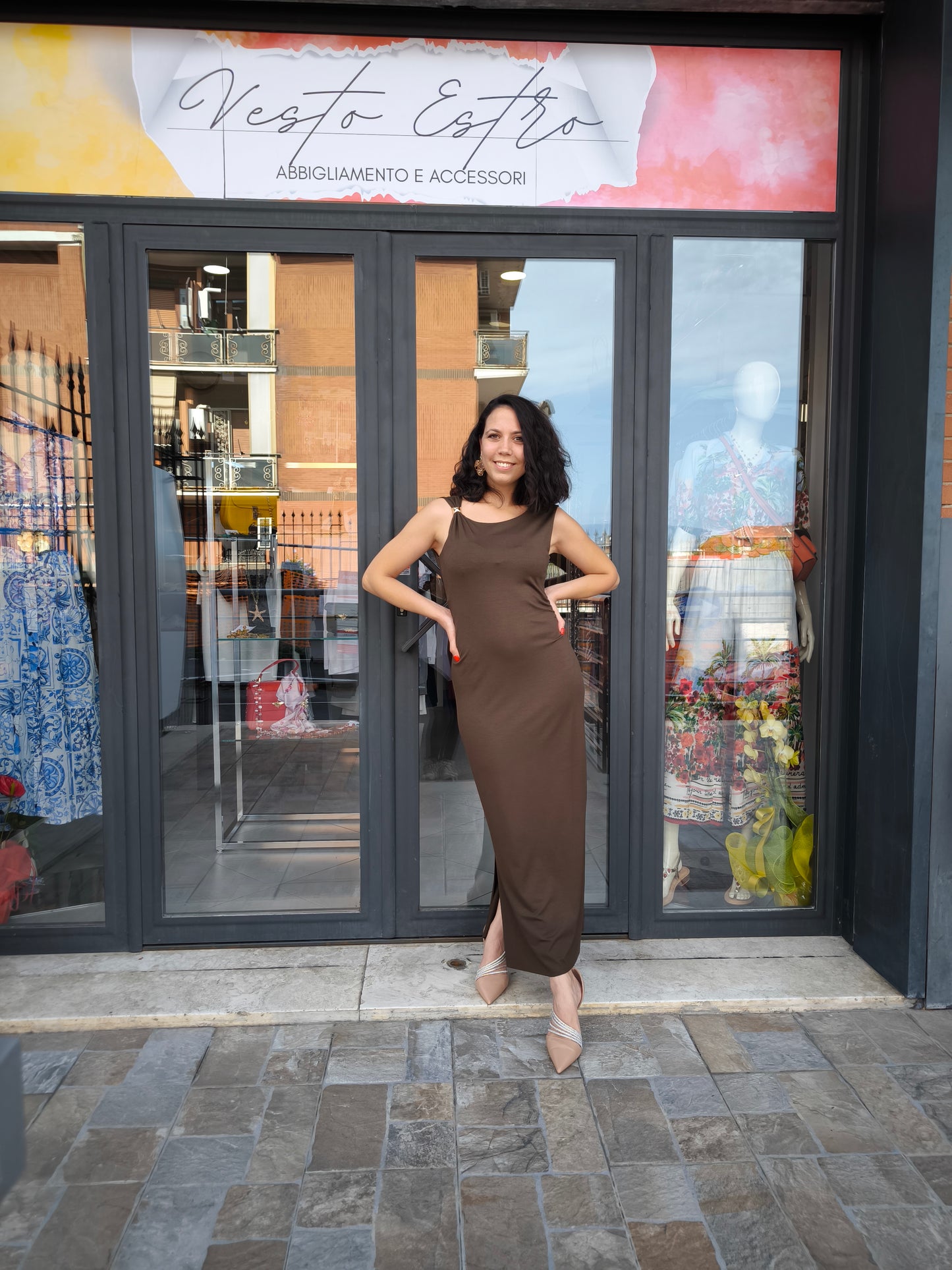 Abito lungo marrone elegante con arricciature laterali e due spacchi, appeso su gruccia in una boutique.