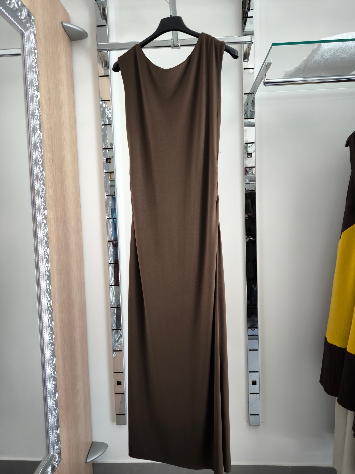Abito lungo marrone elegante con arricciature laterali e due spacchi, appeso su gruccia in una boutique.