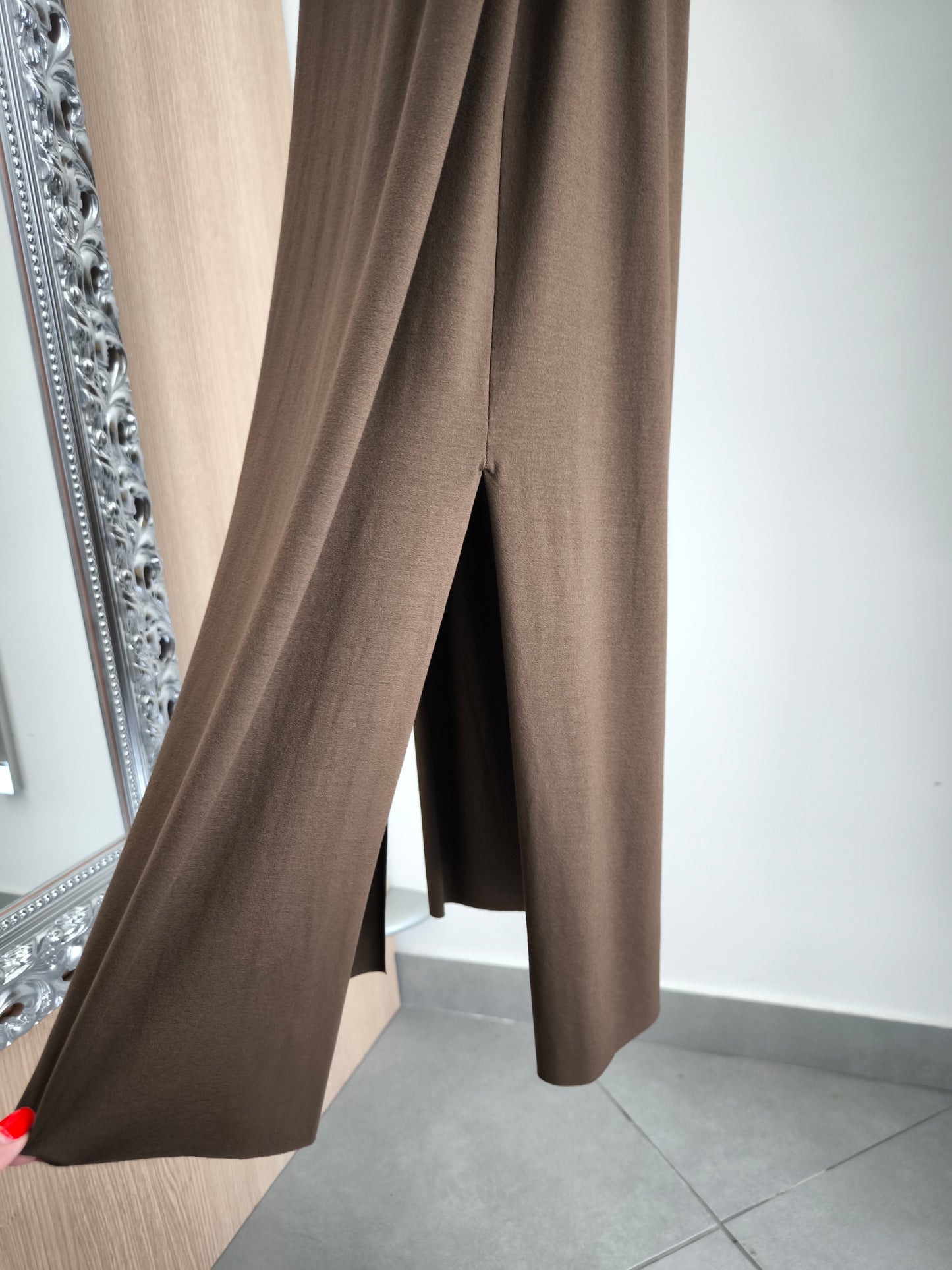Abito lungo marrone elegante con arricciature laterali e due spacchi, appeso su gruccia in una boutique.