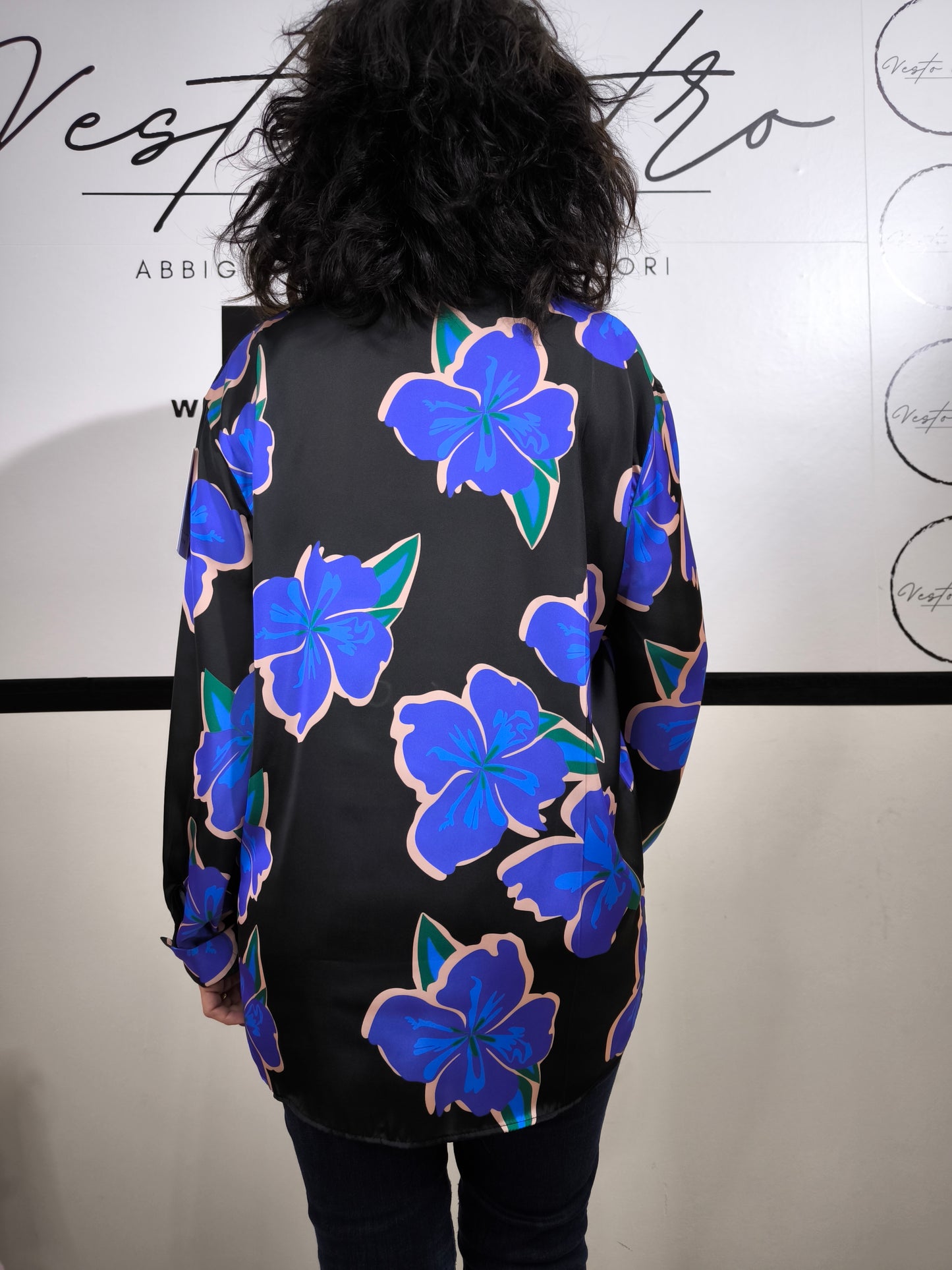 Camicia da donna nera con grandi fiori blu e rosa, stile floreale moderno, indossata con jeans.