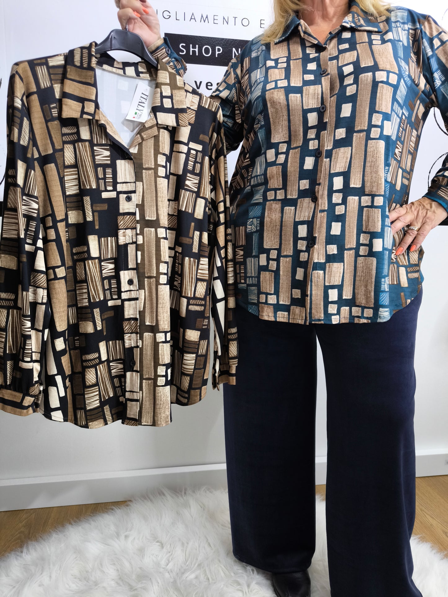 Donna che indossa una camicia in viscosa blu petrolio con stampa geometrica, affiancata dalla stessa camicia in tonalità nera e dorata su appendino.