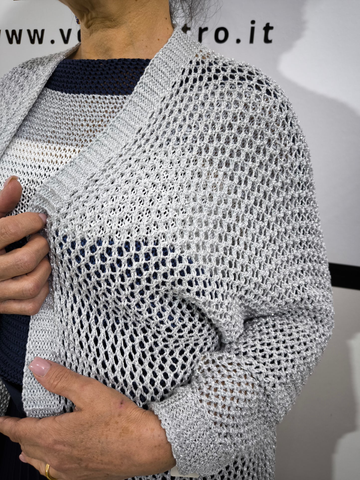 Cardigan aperto traforato in tessuto leggero con fili lurex argentati, abbinato a un top blu e gonna plissettata per un look raffinato.