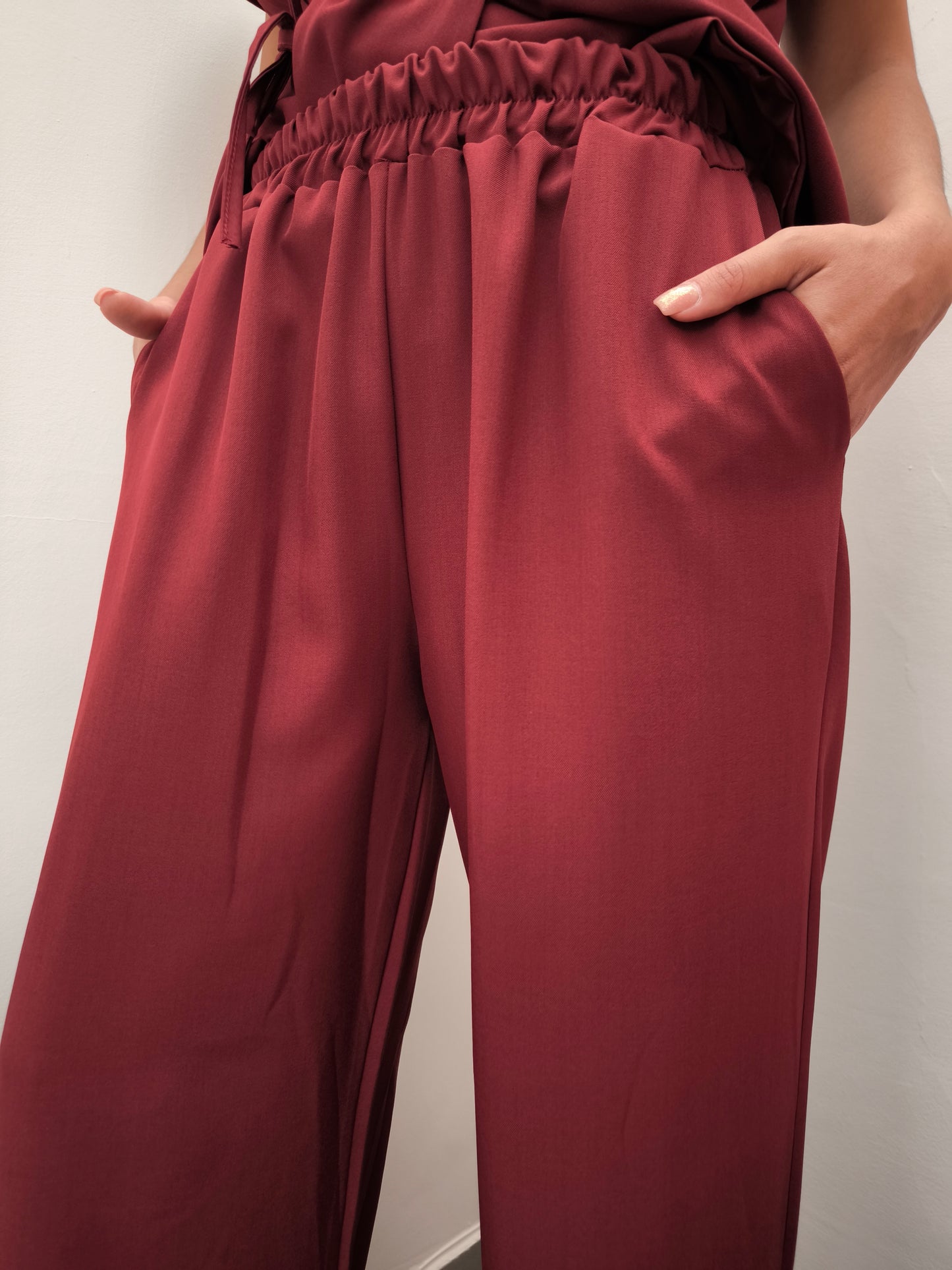 Donna che indossa completo elegante AURA in tessuto bordeaux, con pantaloni larghi.