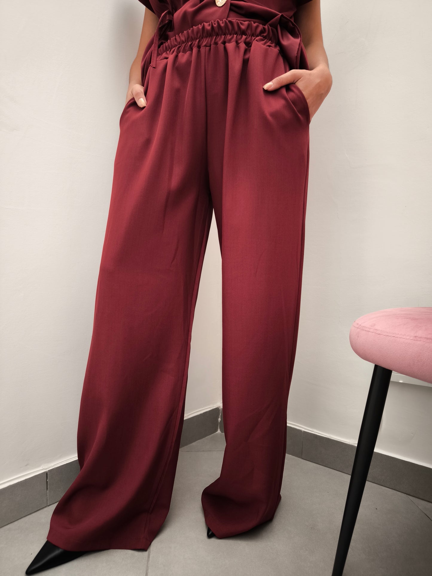 Donna che indossa completo elegante AURA in tessuto bordeaux, con pantaloni larghi.