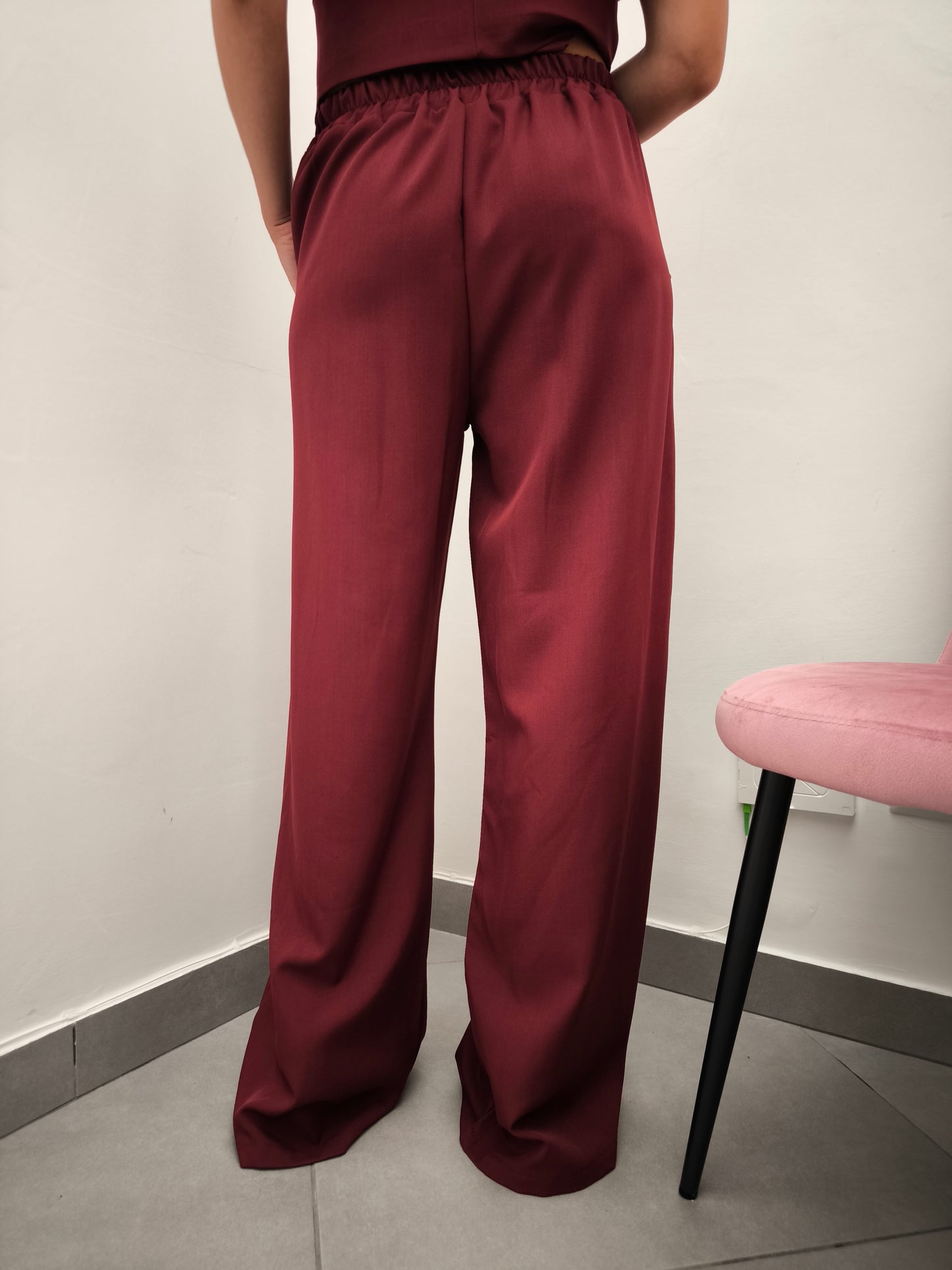 Donna che indossa completo elegante AURA in tessuto bordeaux, con pantaloni larghi.