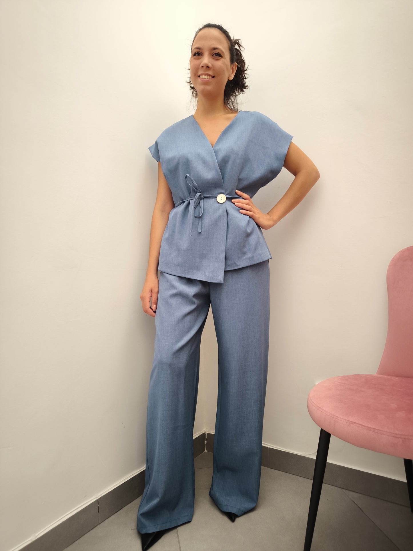 Donna che indossa completo elegante AURA in tessuto denim, con giacca foderata a manica corta e pantaloni larghi.