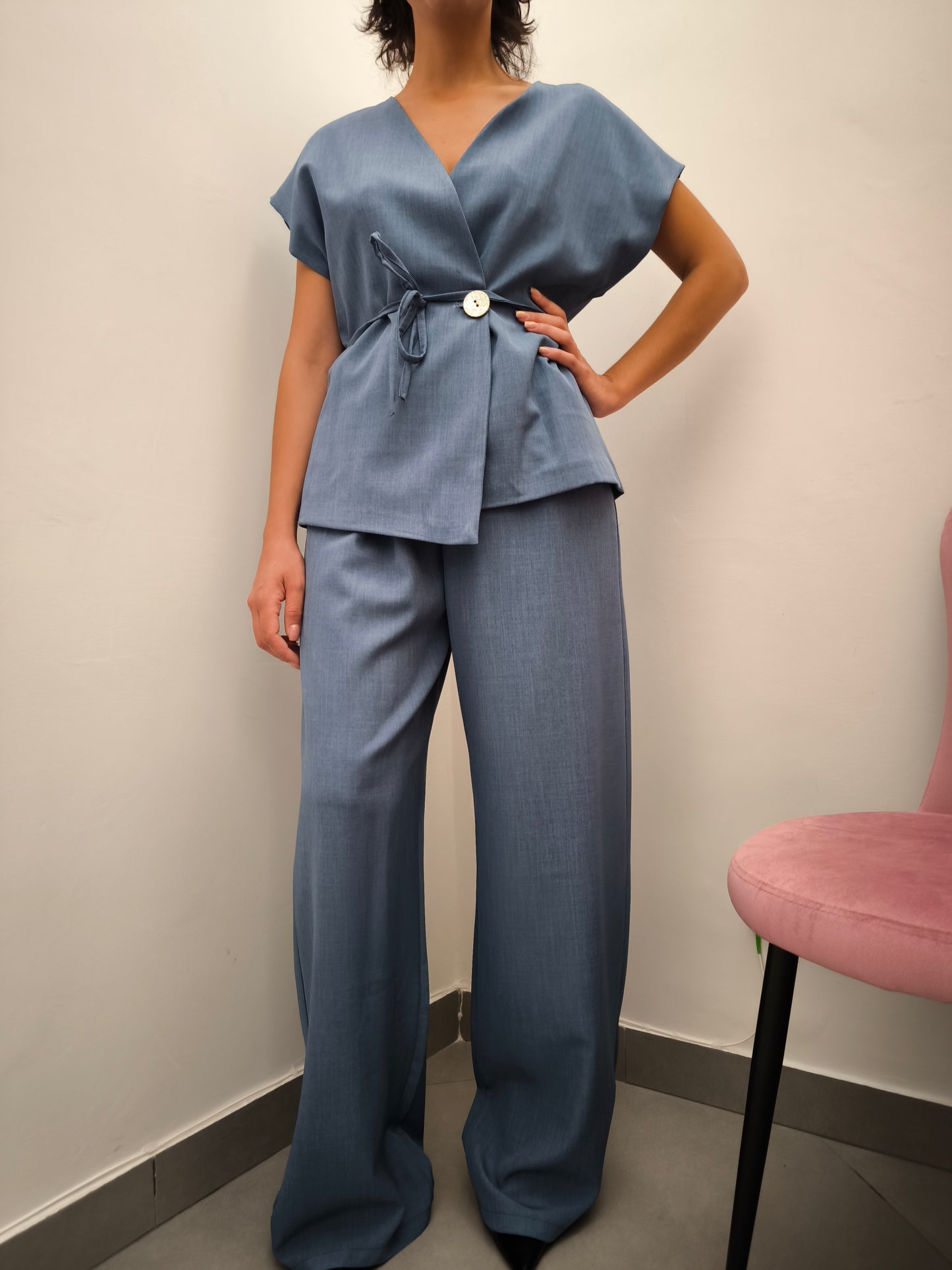 Donna che indossa completo elegante AURA in tessuto denim, con giacca foderata a manica corta e pantaloni larghi.