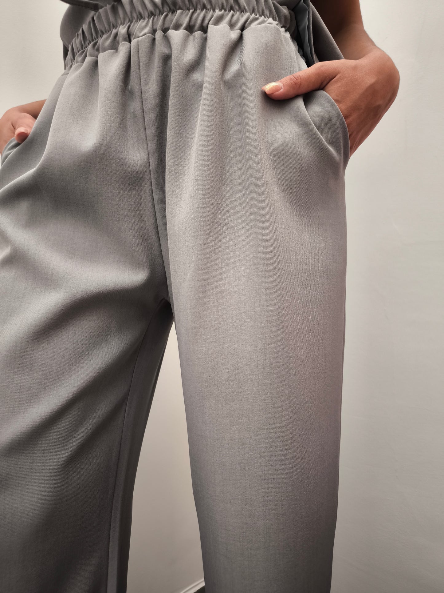 Donna che indossa completo elegante AURA in tessuto grigio, con pantaloni larghi.