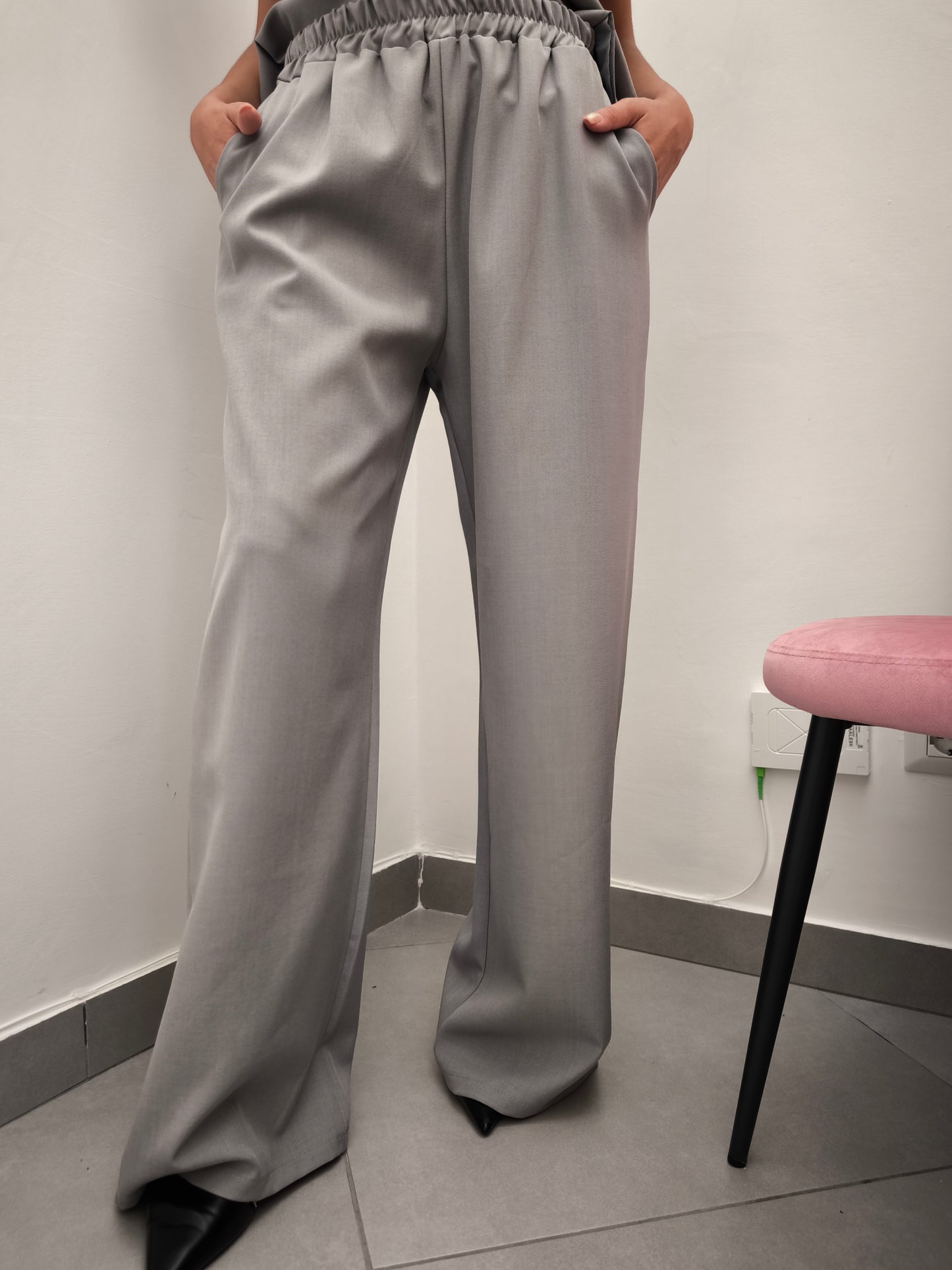 Donna che indossa completo elegante AURA in tessuto grigio, con pantaloni larghi.