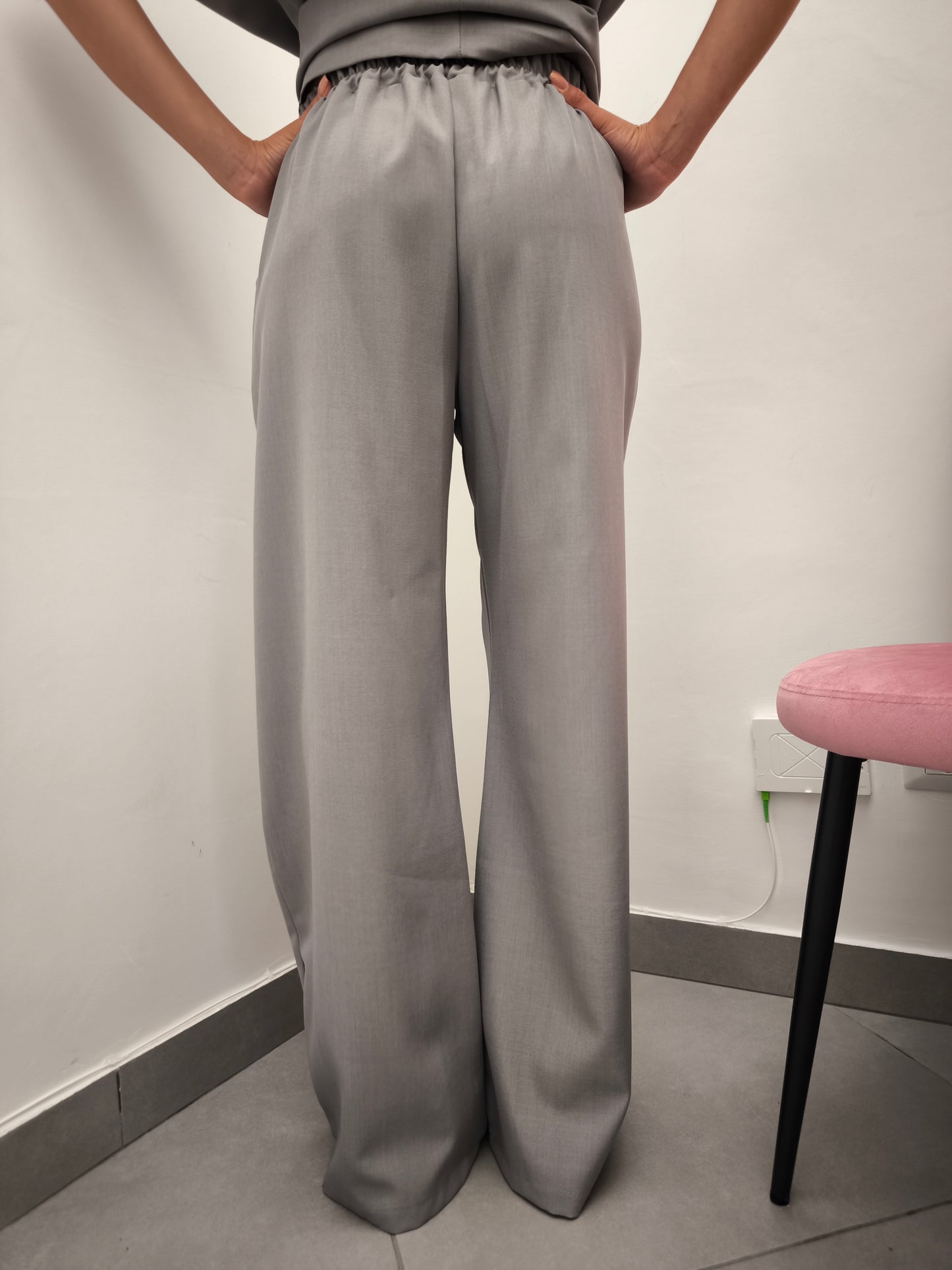 Donna che indossa completo elegante AURA in tessuto grigio, con pantaloni larghi.