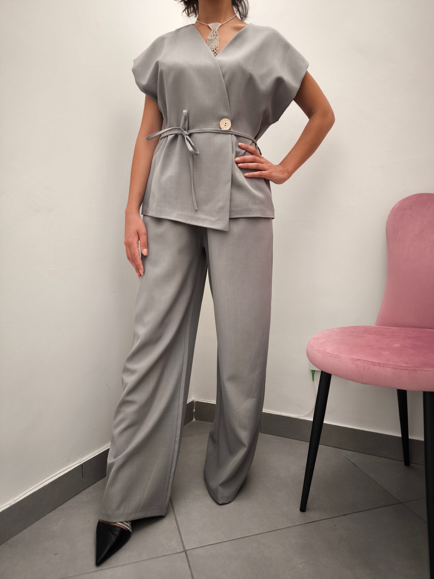 Donna che indossa completo elegante AURA in tessuto grigio, con giacca foderata a manica corta e pantaloni larghi.