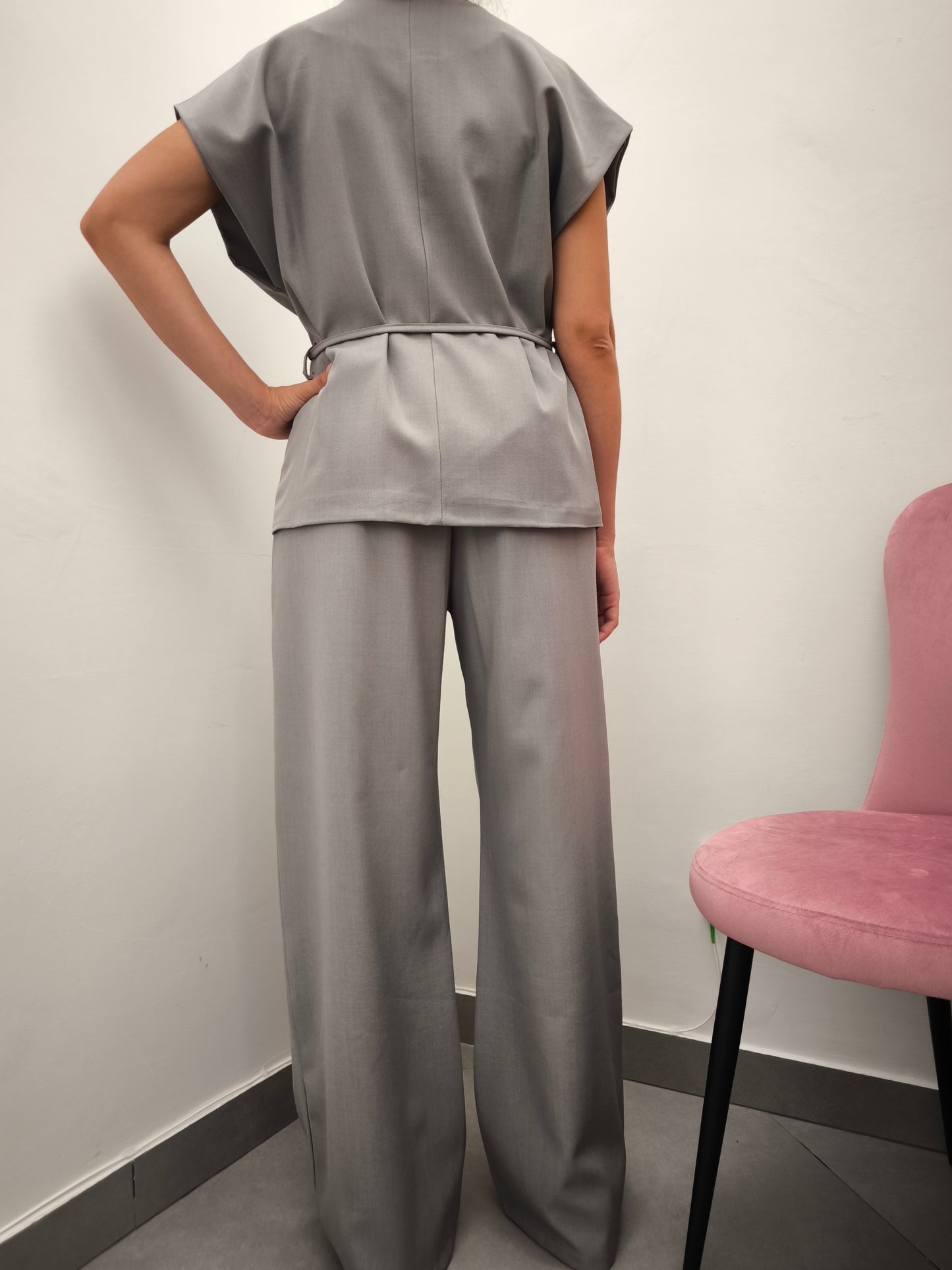 Donna che indossa completo elegante AURA in tessuto grigio, con giacca foderata a manica corta e pantaloni larghi.