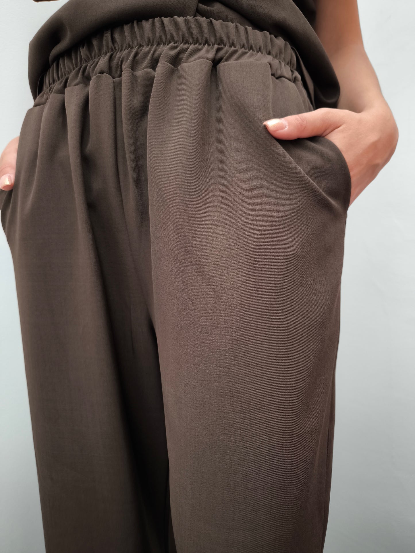 Donna che indossa completo elegante AURA in tessuto marrone, con pantaloni larghi.