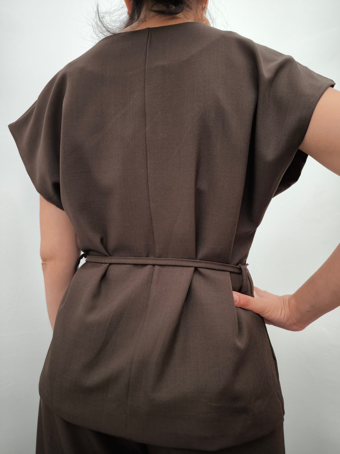 Donna che indossa completo elegante AURA in tessuto marrone, con giacca foderata a manica corta