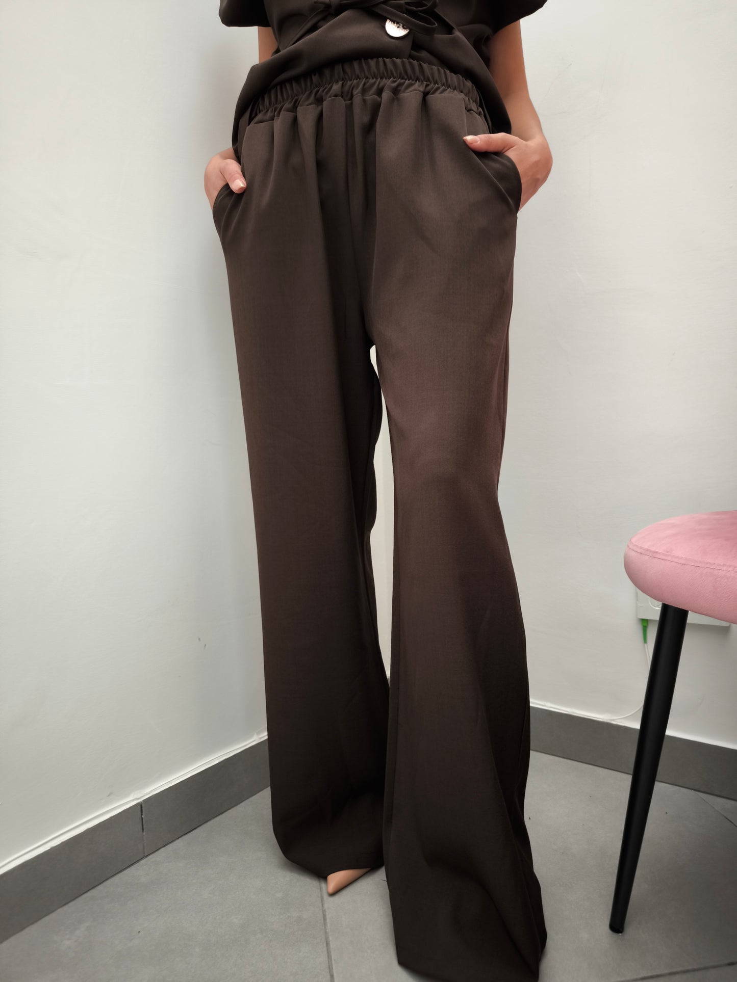 Donna che indossa completo elegante AURA in tessuto marrone, con pantaloni larghi.