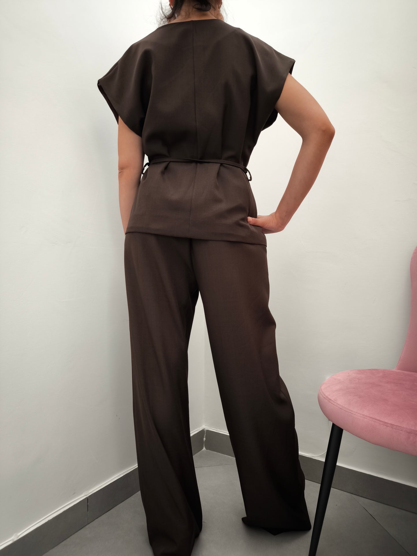 Donna che indossa completo elegante AURA in tessuto marrone, con giacca foderata a manica corta e pantaloni larghi.