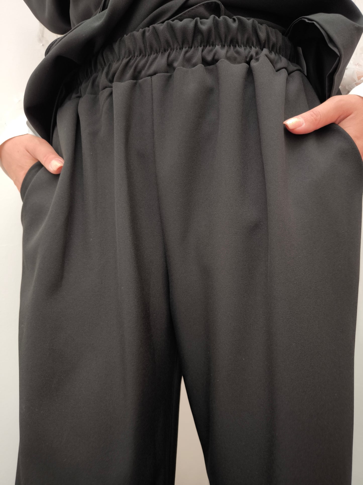 Donna che indossa completo elegante AURA in tessuto nero, con pantaloni larghi.