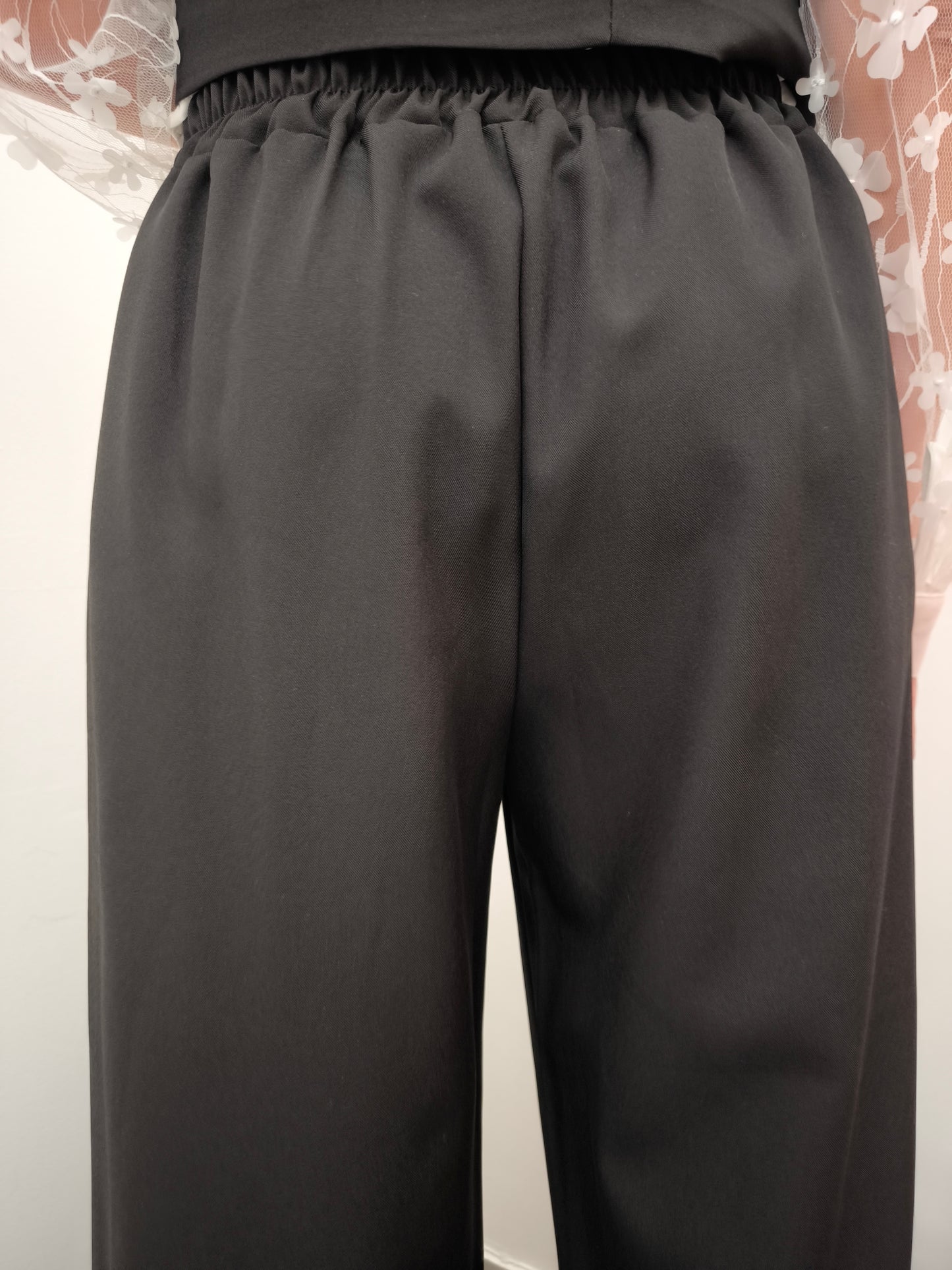 Donna che indossa completo elegante AURA in tessuto nero, con pantaloni larghi.