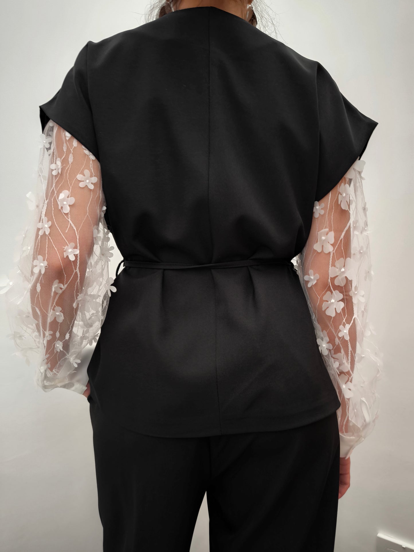Donna che indossa completo elegante AURA in tessuto nero, con giacca foderata a manica corta