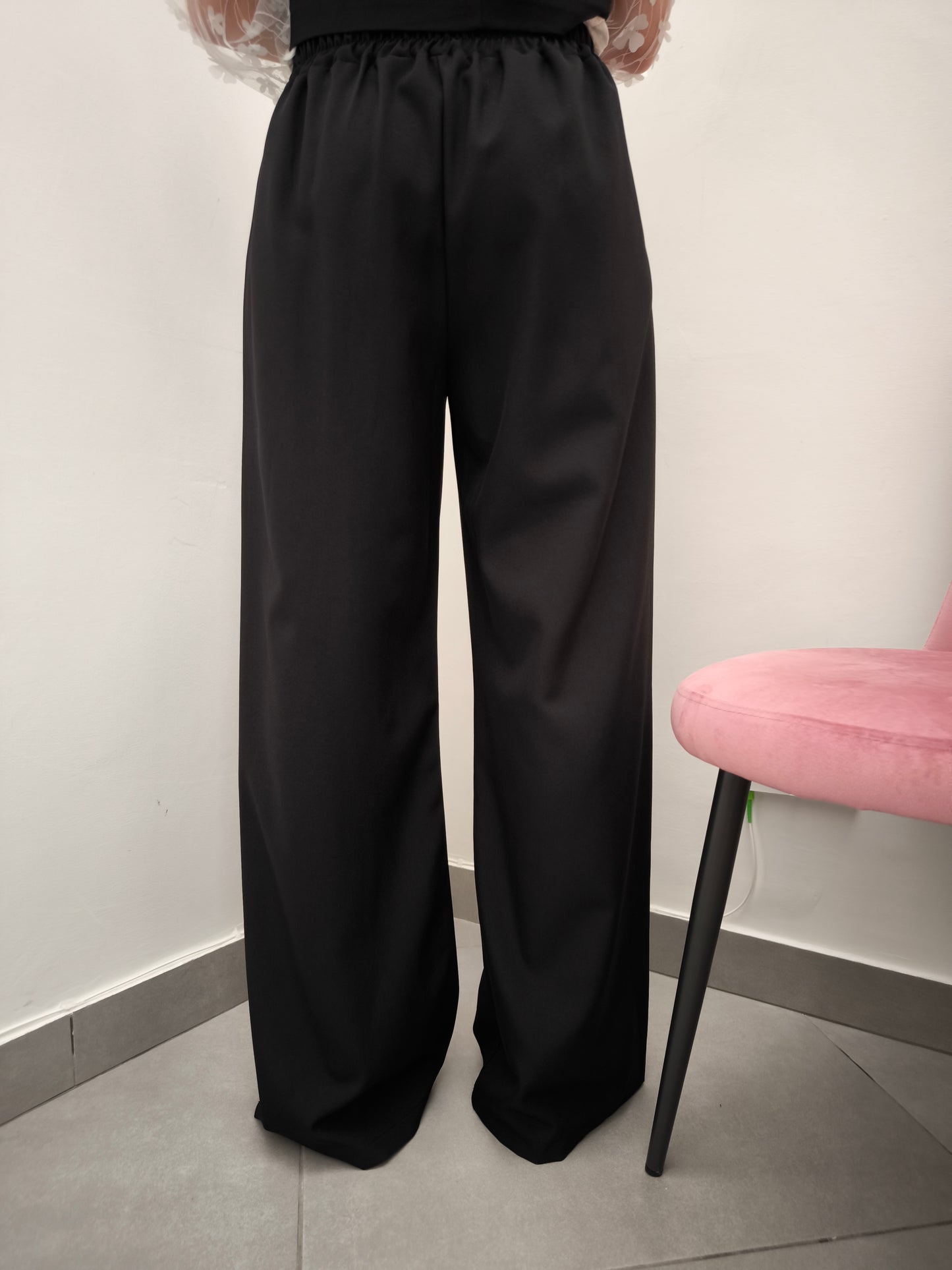 Donna che indossa completo elegante AURA in tessuto nero, con pantaloni larghi.