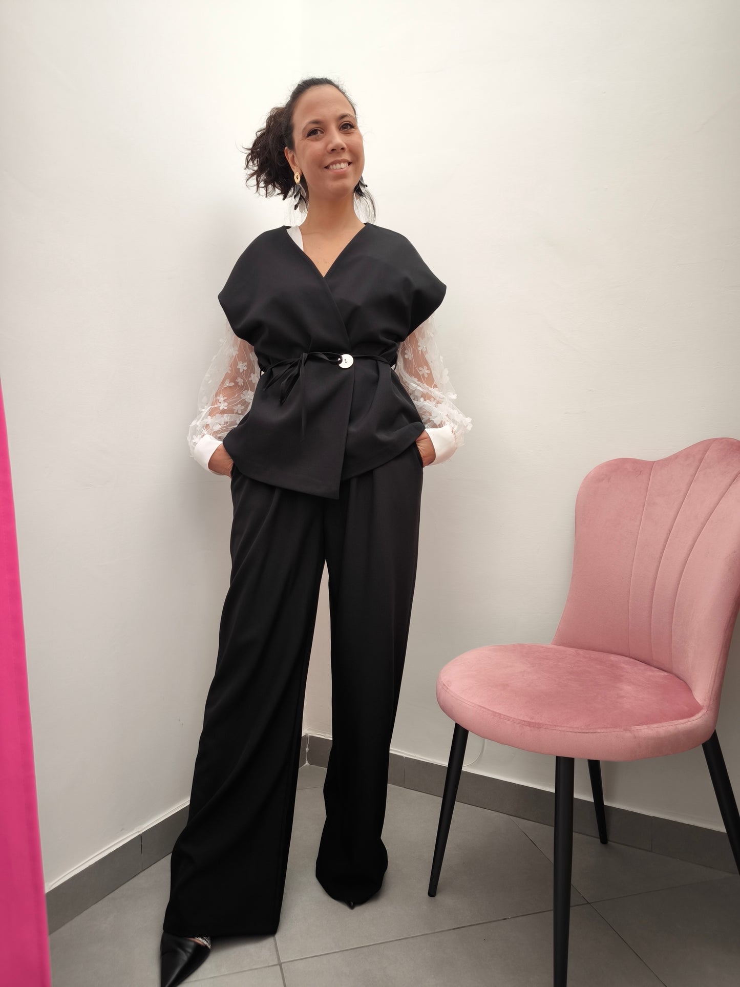 Donna che indossa completo elegante AURA in tessuto nero, con giacca foderata a manica corta e pantaloni larghi.
