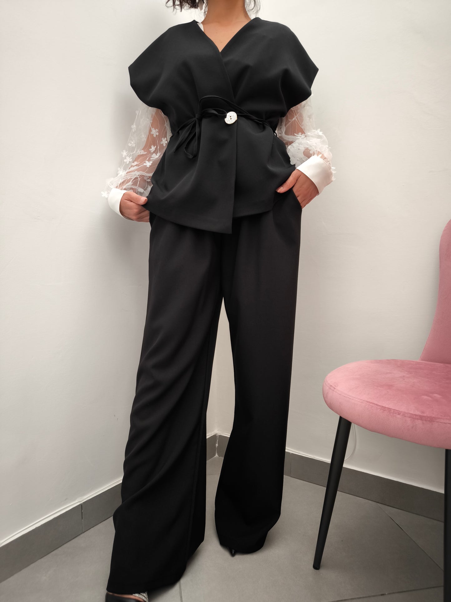Donna che indossa completo elegante AURA in tessuto nero, con giacca foderata a manica corta e pantaloni larghi.