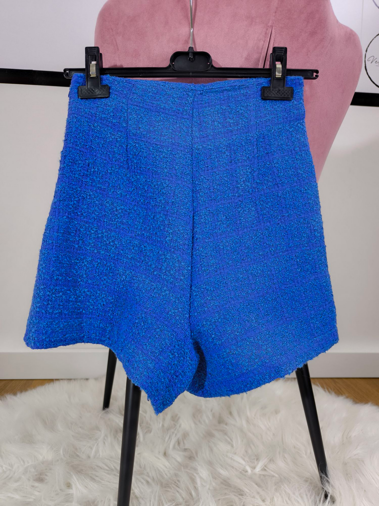 Gonna pantaloncino corta in tessuto tweed blu con dettaglio a bottoni e design avvolgente, perfetta per un look casual chic ed elegante.