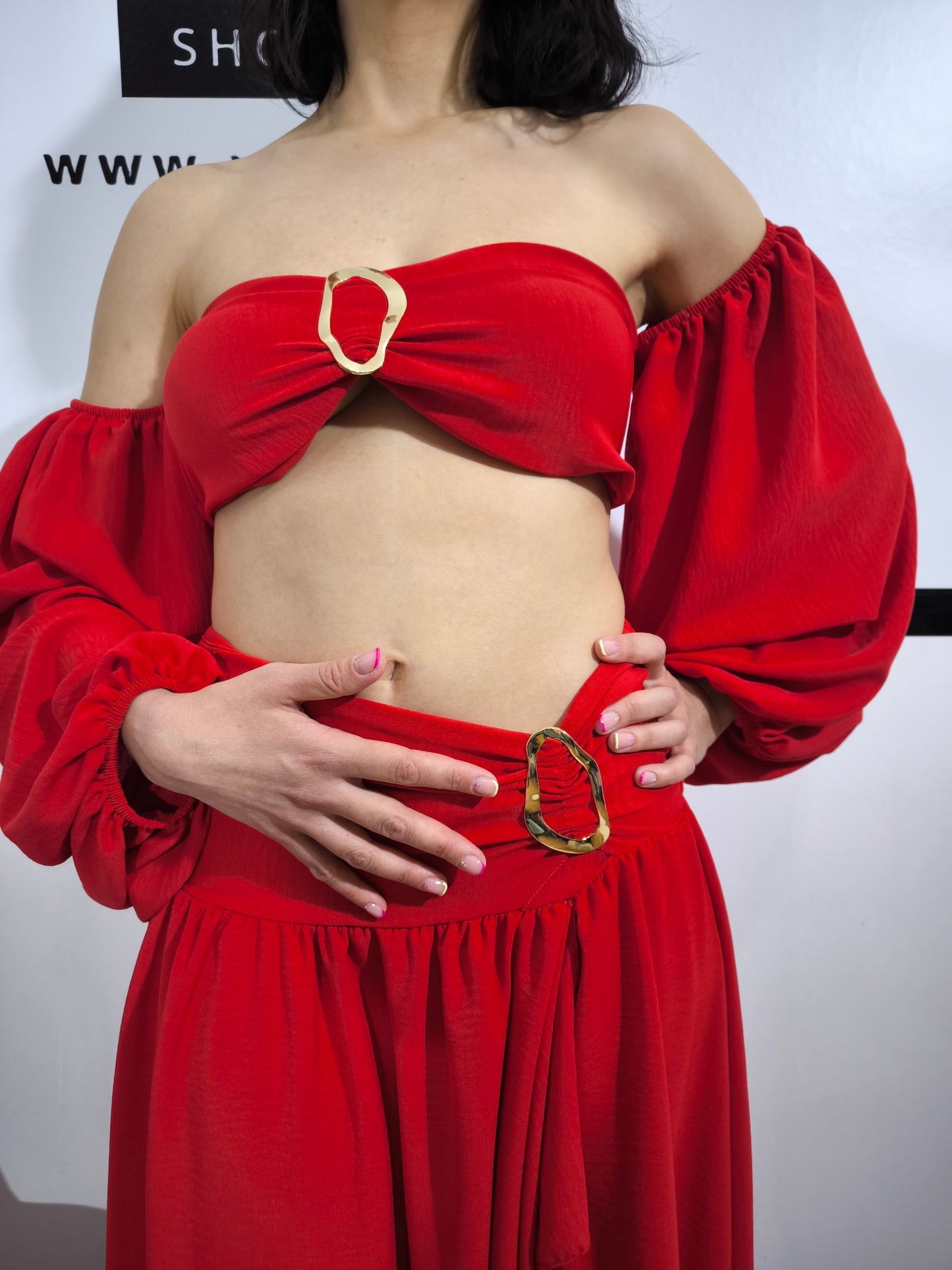 Donna indossa un completo rosso con top a fascia con maniche a palloncino e gonna lunga con spacco laterale – outfit elegante Vesto Estro.