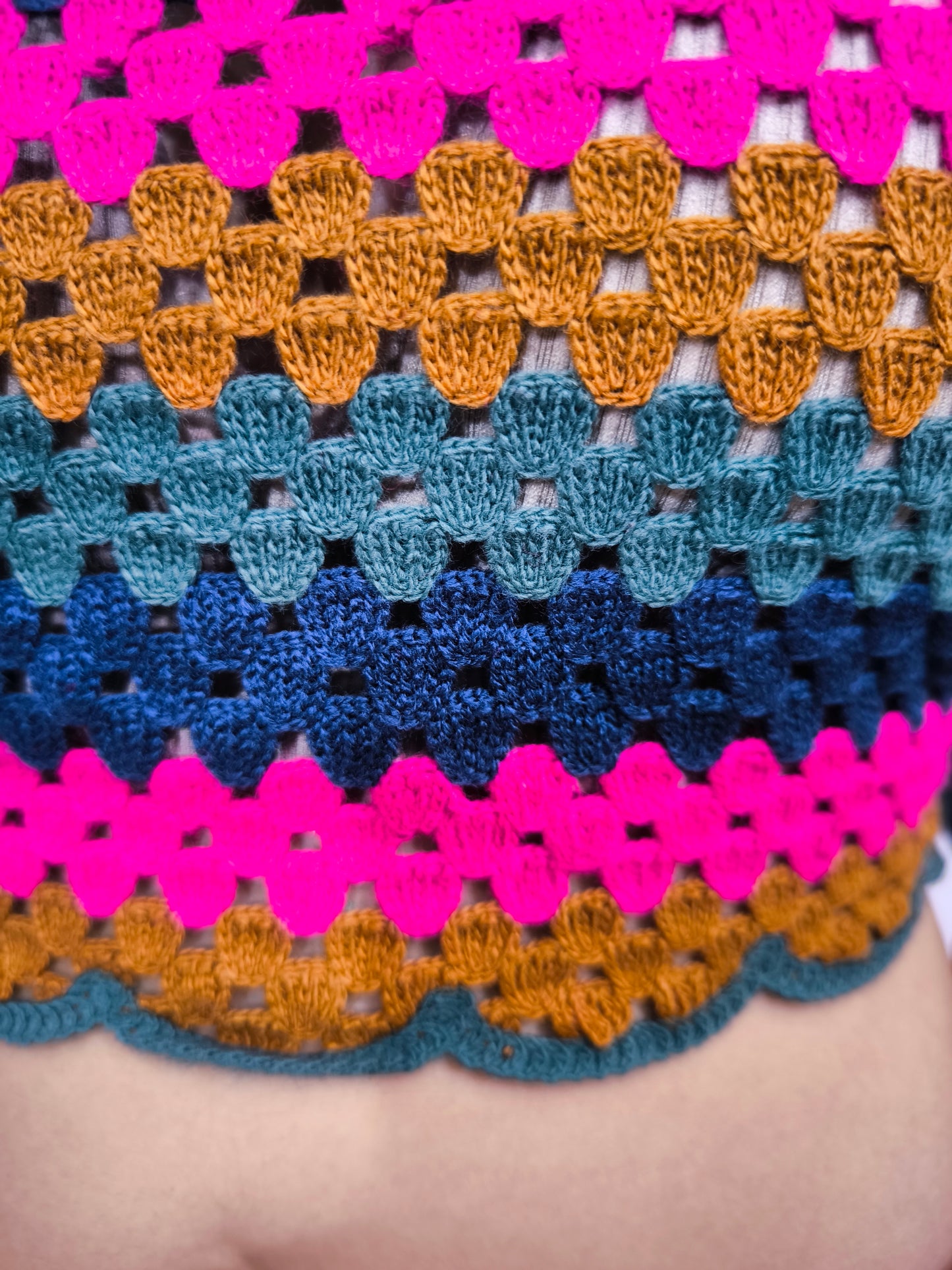 Maglia crochet multicolor a righe con schiena incrociata, abbinata a pantaloni fucsia e cintura dorata, indossata da una modella sorridente.