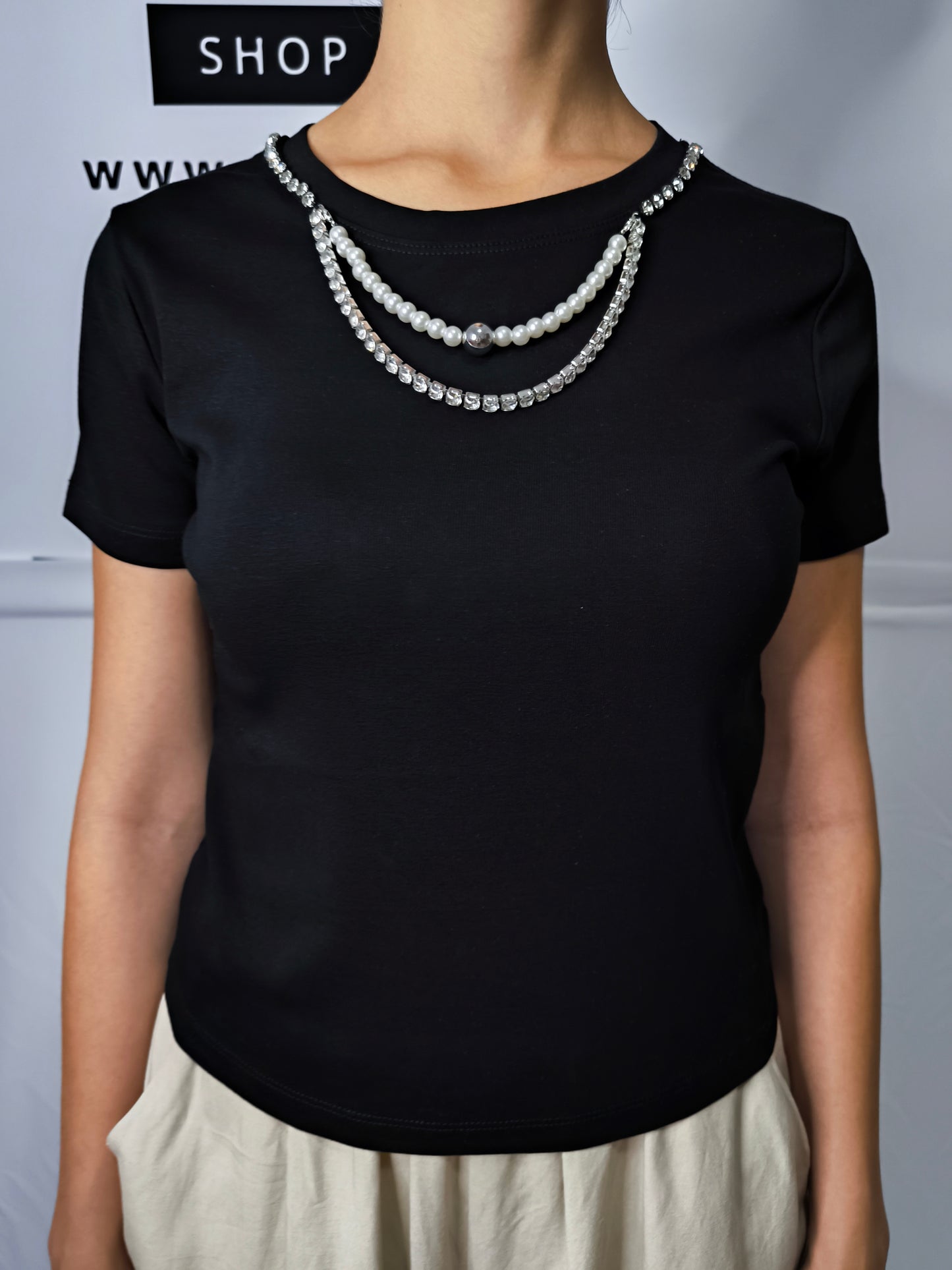 T-shirt nera da donna con girocollo decorato da collana di perle e strass, elegante e versatile per look casual chic.