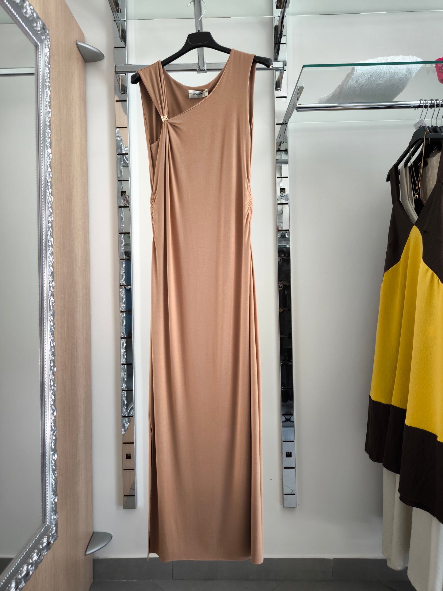 Abito lungo beige elegante con arricciature laterali e due spacchi, appeso su gruccia in una boutique.