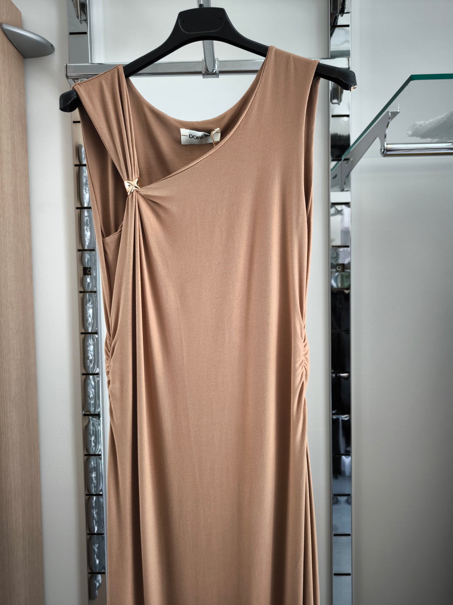 Abito lungo beige elegante con arricciature laterali e due spacchi, appeso su gruccia in una boutique.