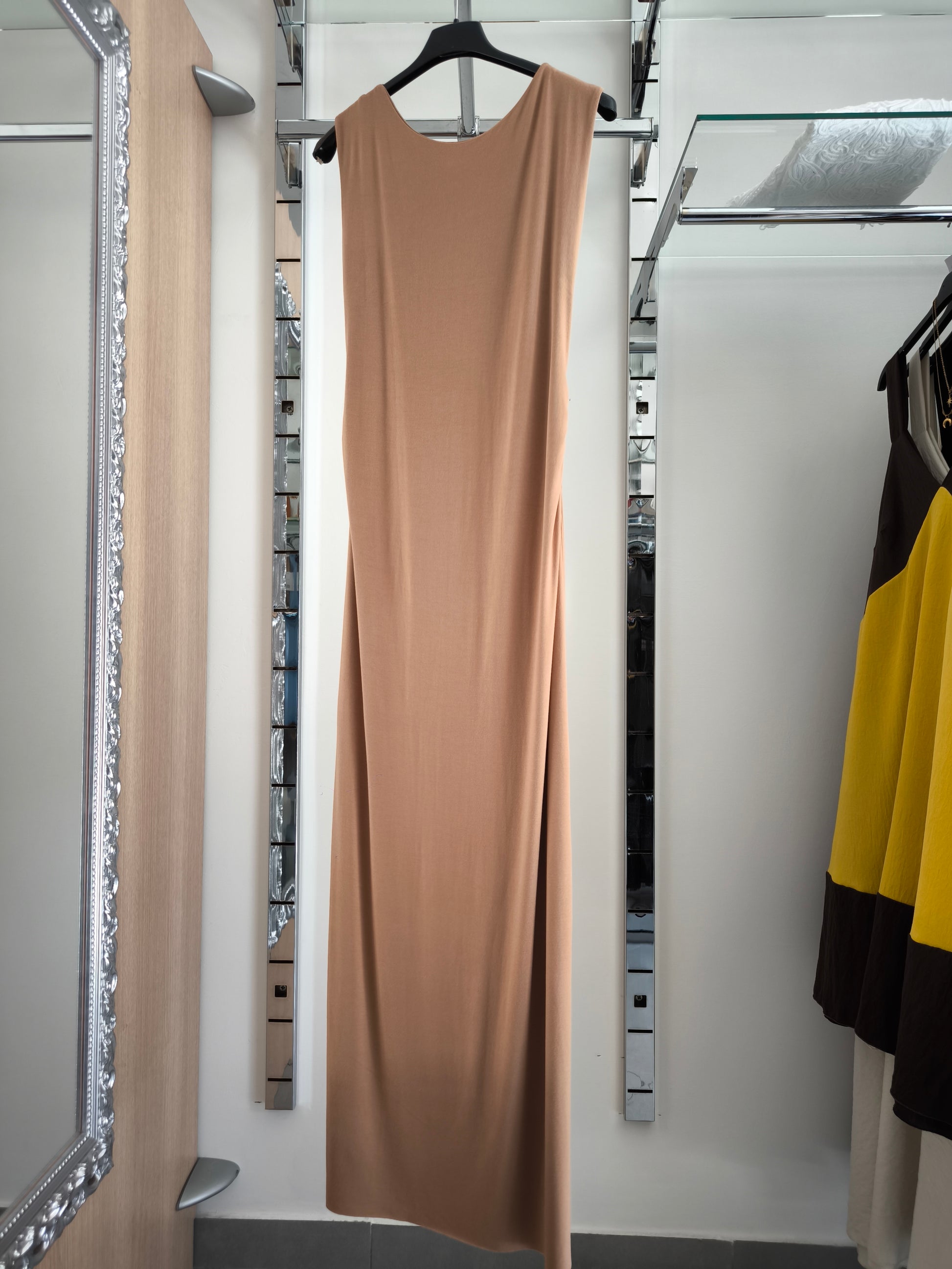 Abito lungo beige elegante con arricciature laterali e due spacchi, appeso su gruccia in una boutique.