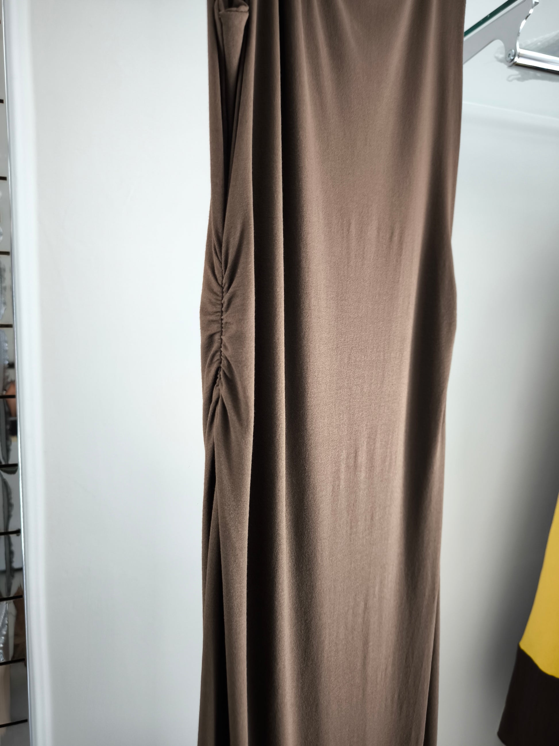 Abito lungo marrone elegante con arricciature laterali e due spacchi, appeso su gruccia in una boutique.