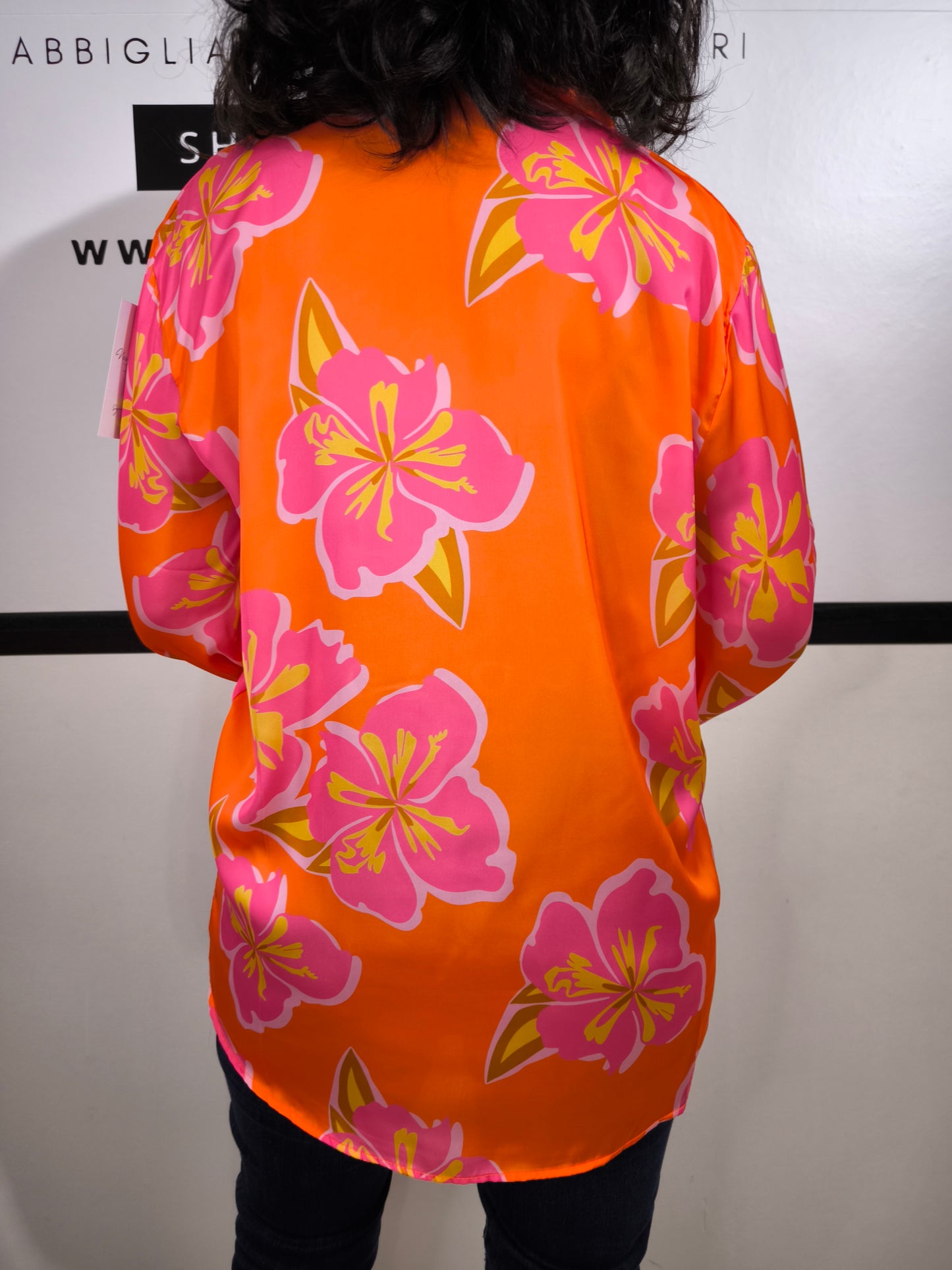 Camicia da donna arancione con grandi fiori rosa e giallo, stile floreale moderno, indossata con jeans.