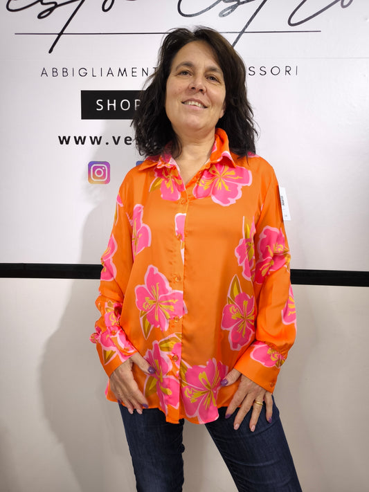 Camicia da donna arancione con grandi fiori rosa e giallo, stile floreale moderno, indossata con jeans.