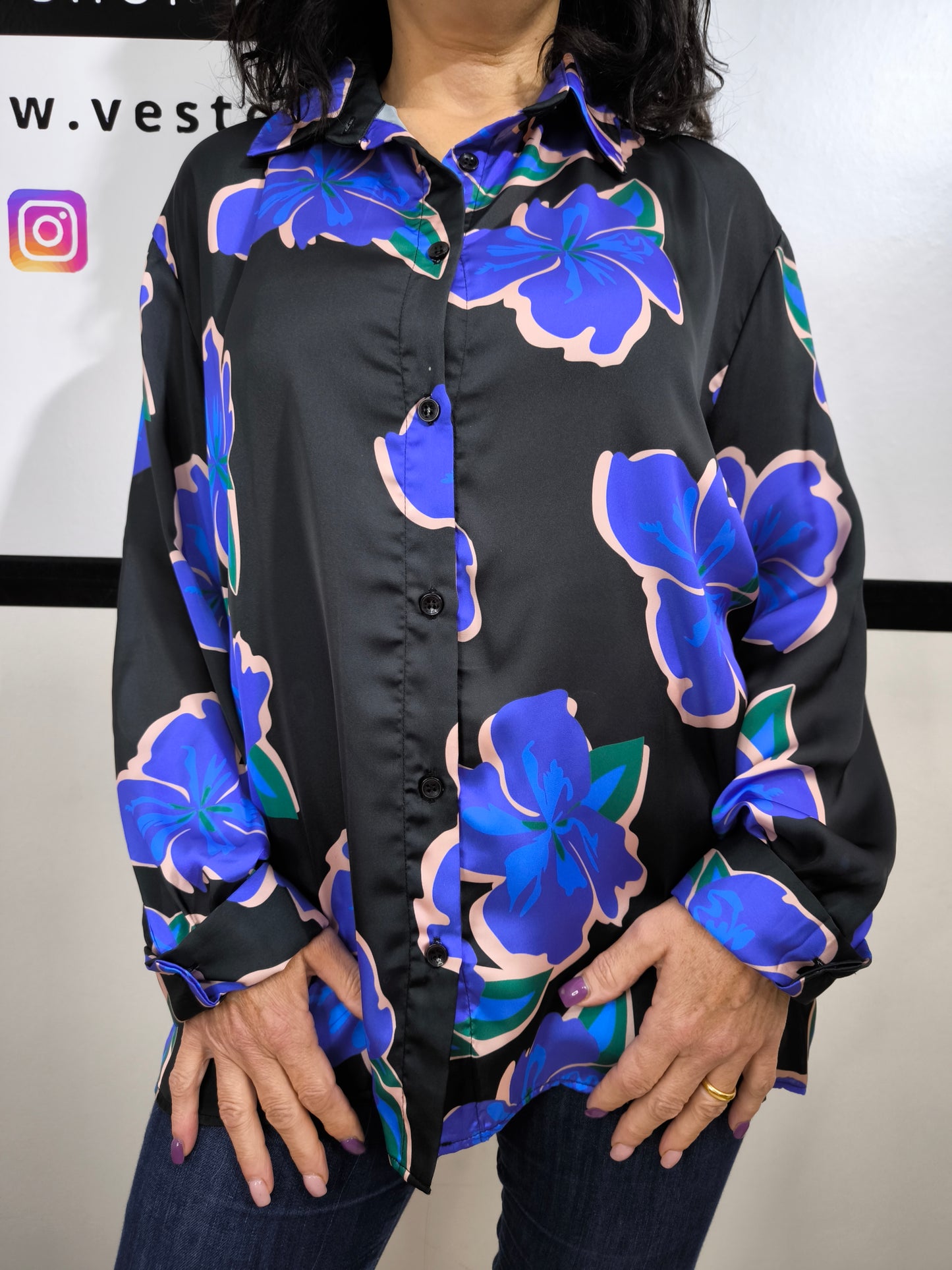 Camicia da donna nera con grandi fiori blu e rosa, stile floreale moderno, indossata con jeans.