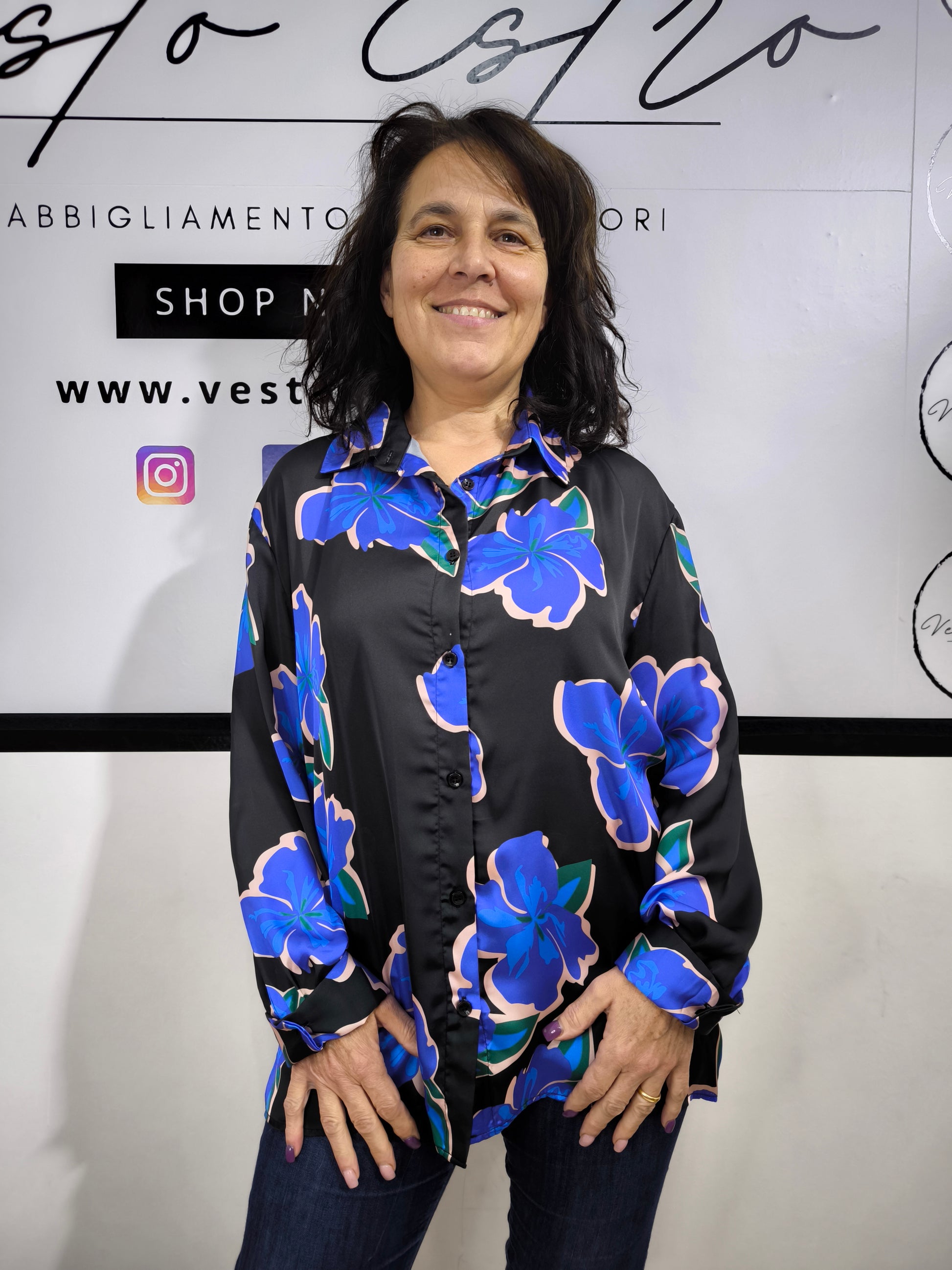 Camicia da donna nera con grandi fiori blu e rosa, stile floreale moderno, indossata con jeans.