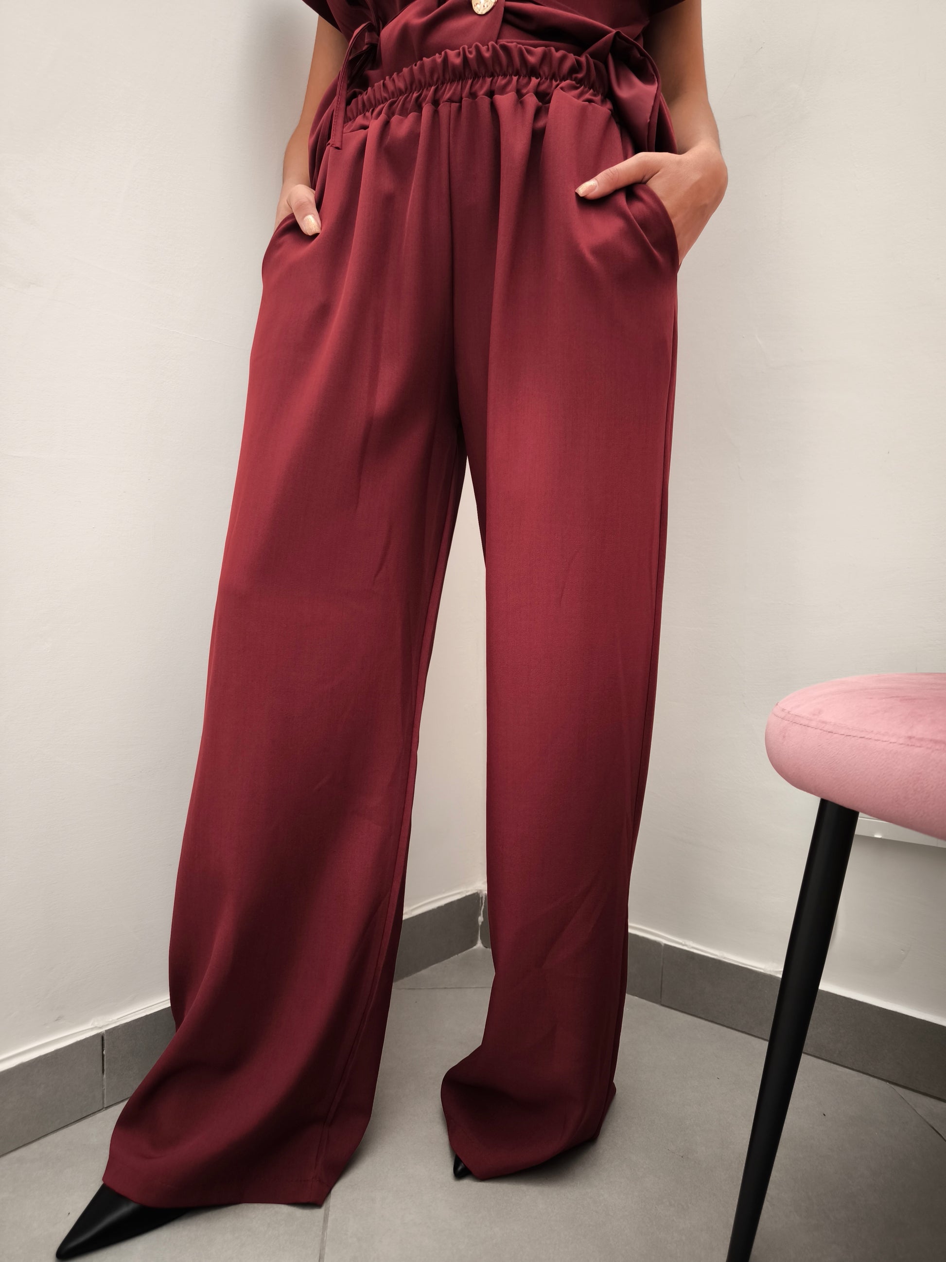 Donna che indossa completo elegante AURA in tessuto bordeaux, con pantaloni larghi.