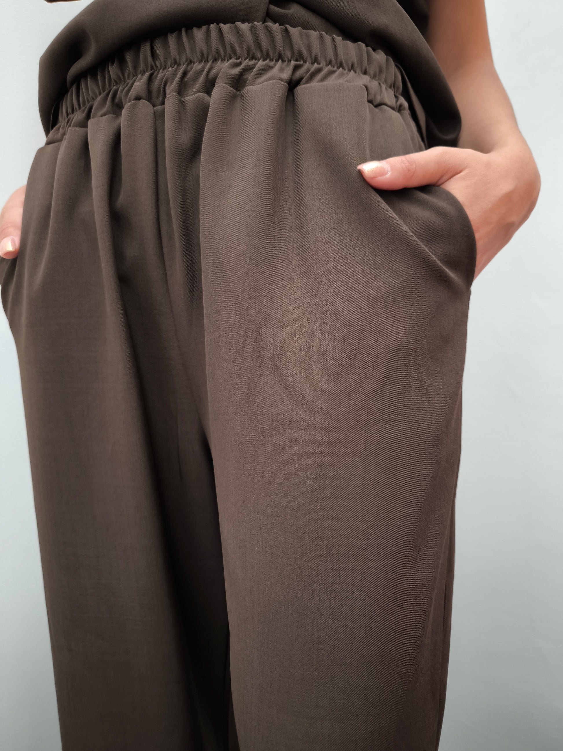 Donna che indossa completo elegante AURA in tessuto marrone, con  pantaloni larghi.