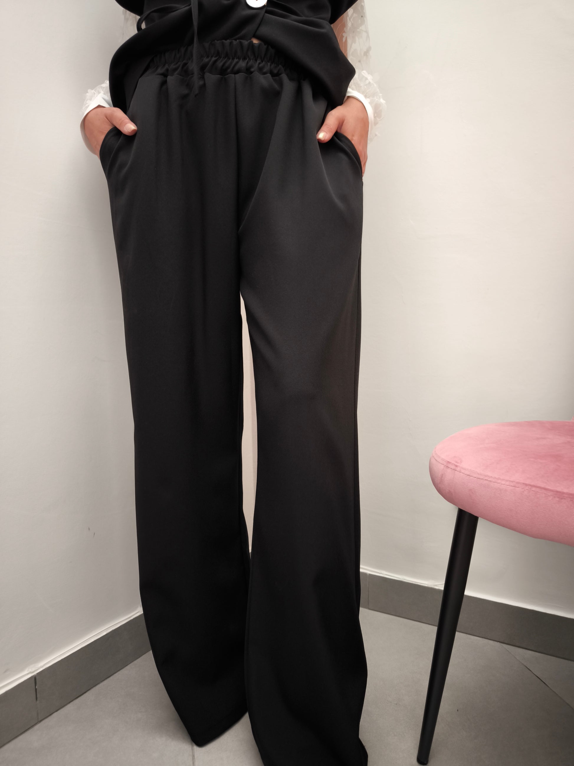 Donna che indossa completo elegante AURA in tessuto nero, con pantaloni larghi.