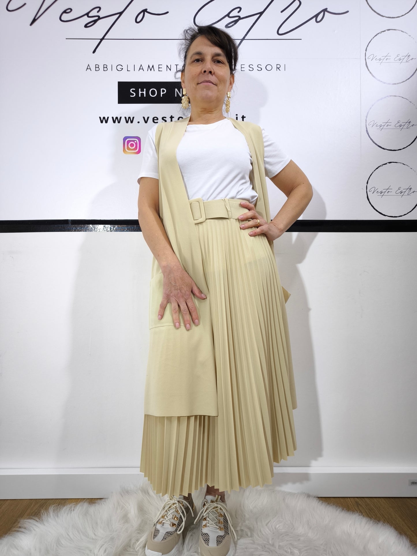 Completo donna con gilet lungo crema e t-shirt bianca, abbinato a gonna plissettata, perfetto per un look casual elegante.