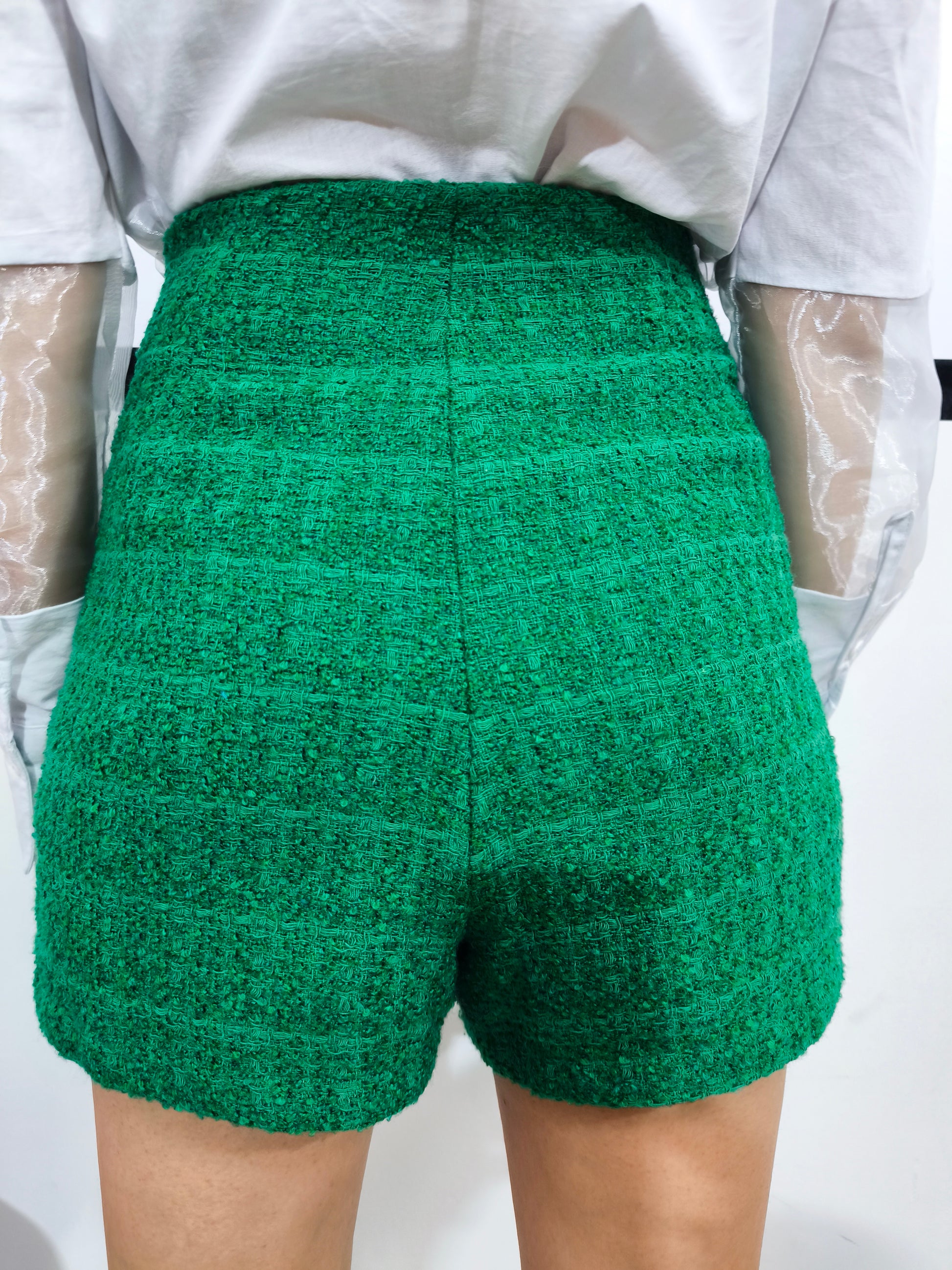 Gonna pantaloncino corta in tessuto tweed verde con dettaglio a bottoni e design avvolgente, perfetta per un look casual chic ed elegante.