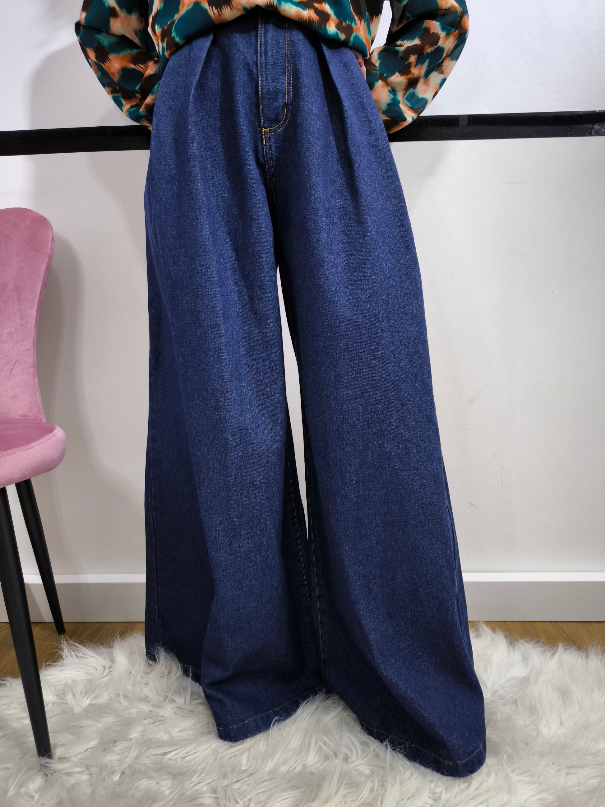 Jeans ampio a vita alta da donna in denim blu, stile palazzo, fotografato su tappeto bianco.