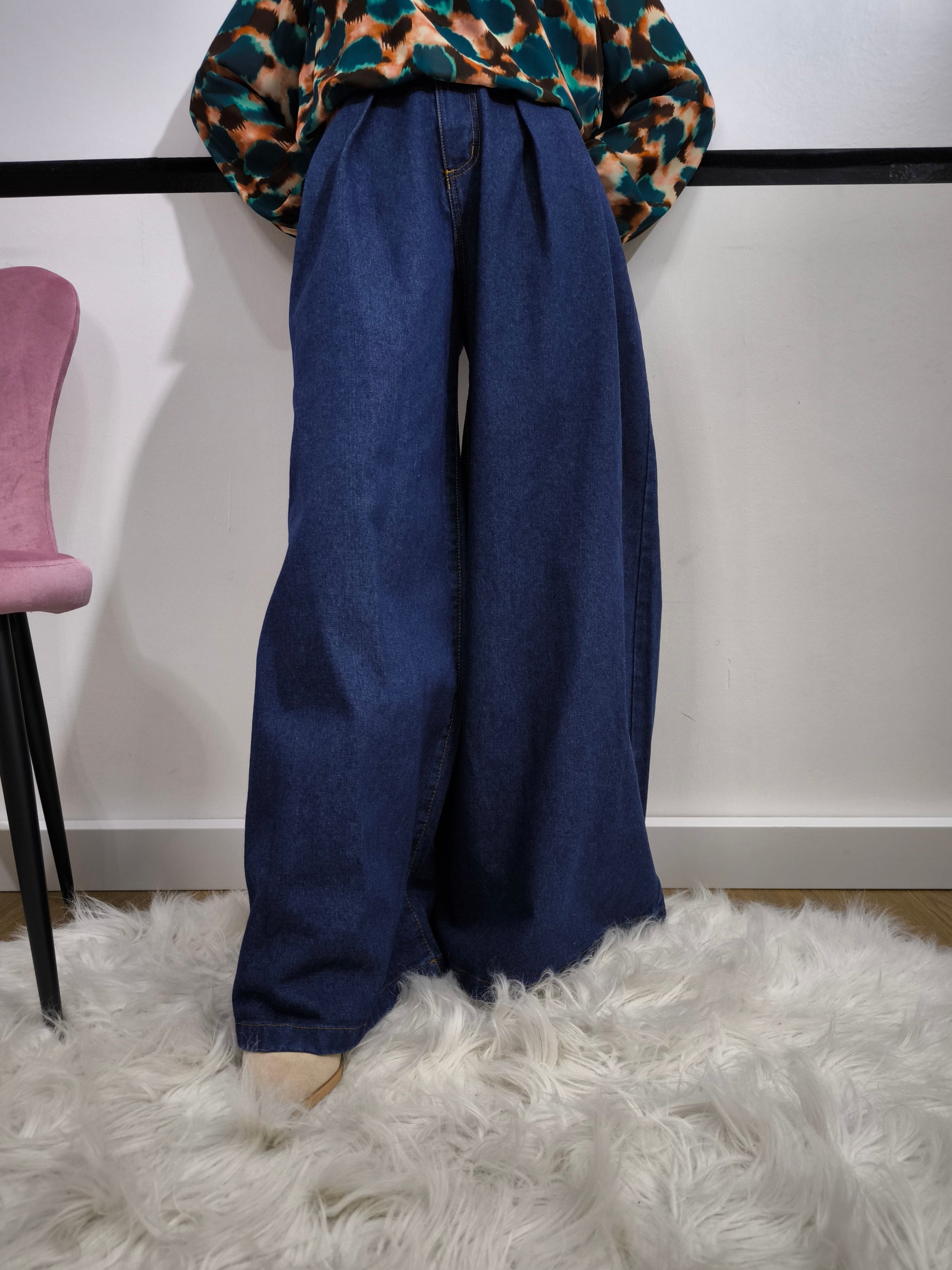Jeans ampio a vita alta da donna in denim blu, stile palazzo, fotografato su tappeto bianco.