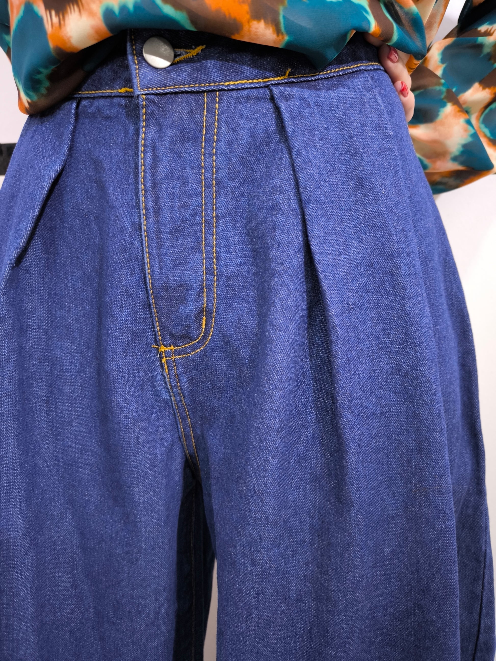 Jeans ampio a vita alta da donna in denim blu, stile palazzo, fotografato su tappeto bianco.
