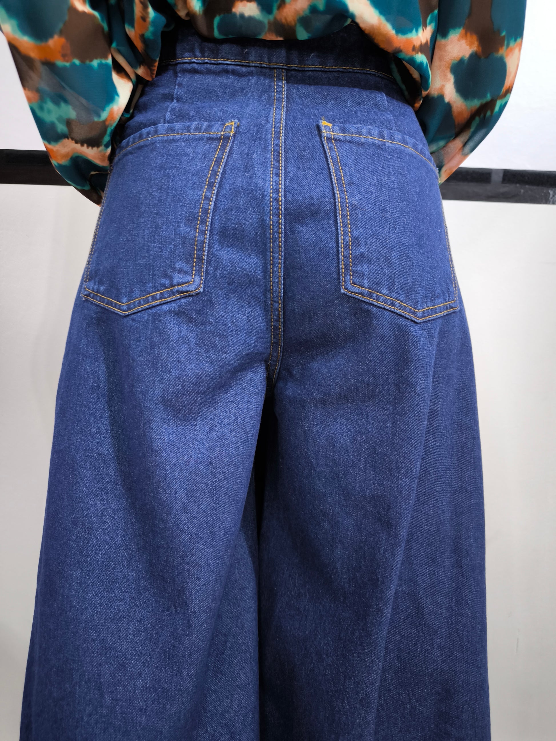 Jeans ampio a vita alta da donna in denim blu, stile palazzo, fotografato su tappeto bianco.