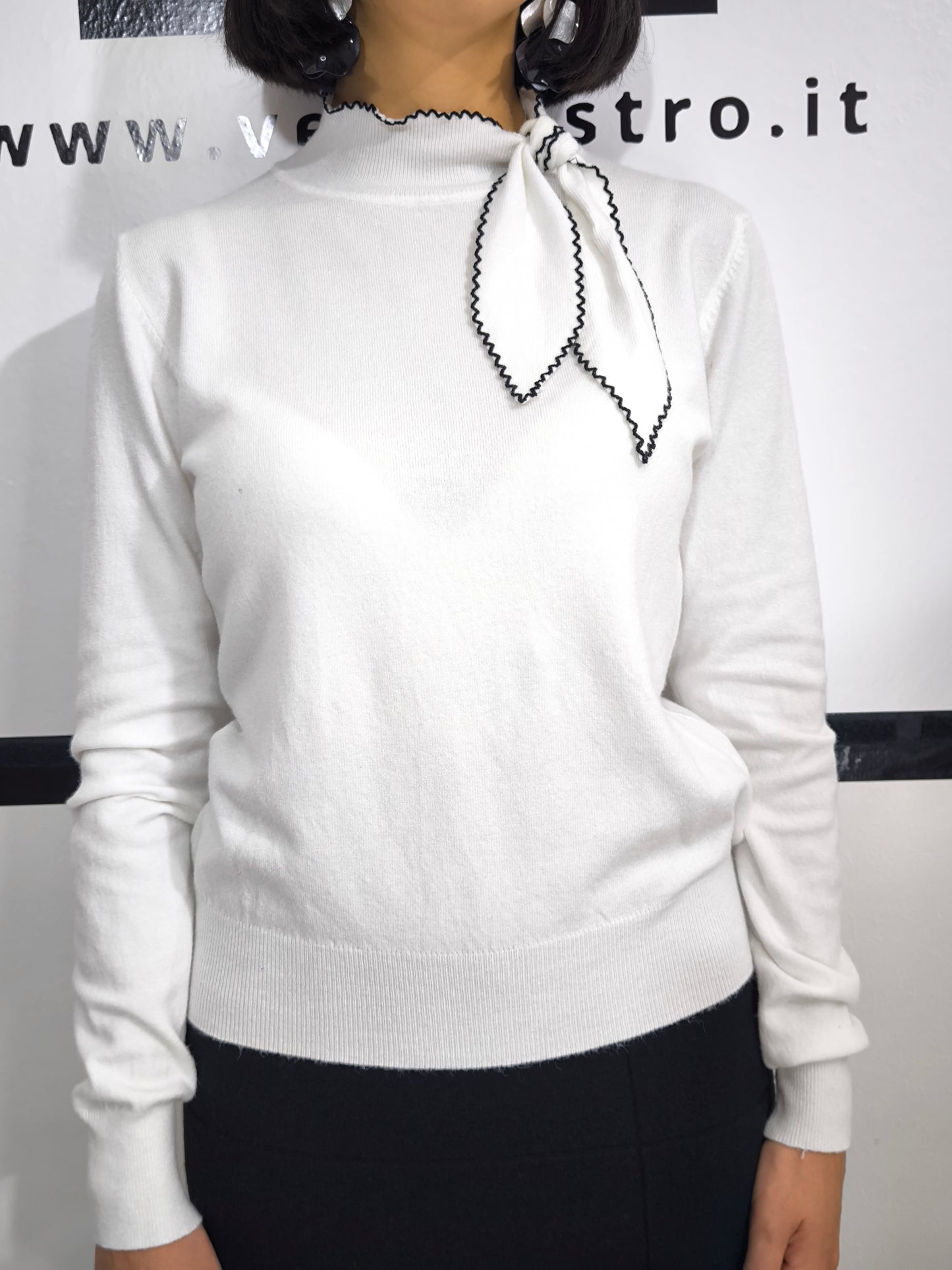 Maglia bianca con fiocco al collo e bordo ricamato in nero, elegante e raffinata.