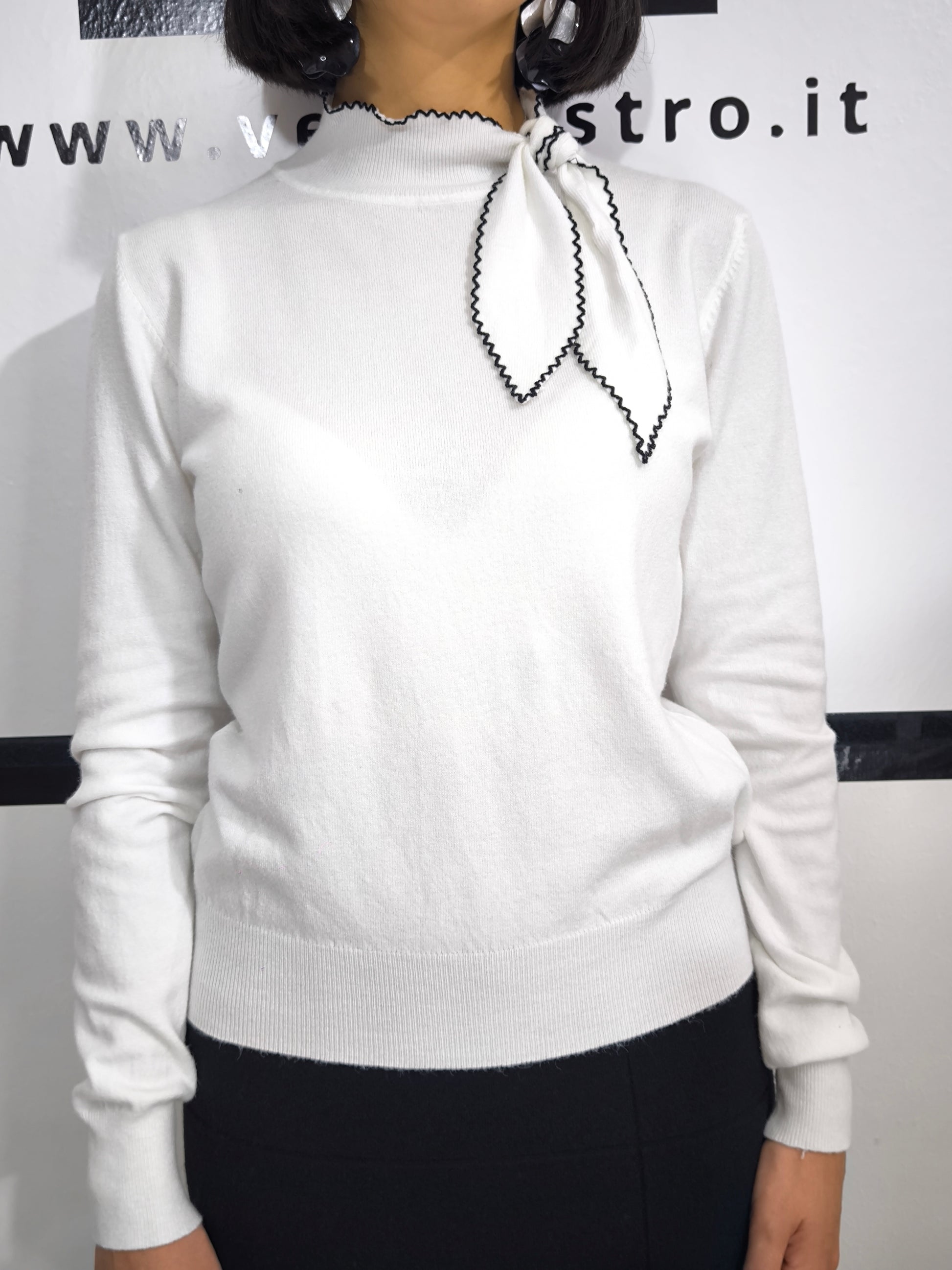 Maglia bianca con fiocco al collo e bordo ricamato in nero, elegante e raffinata.